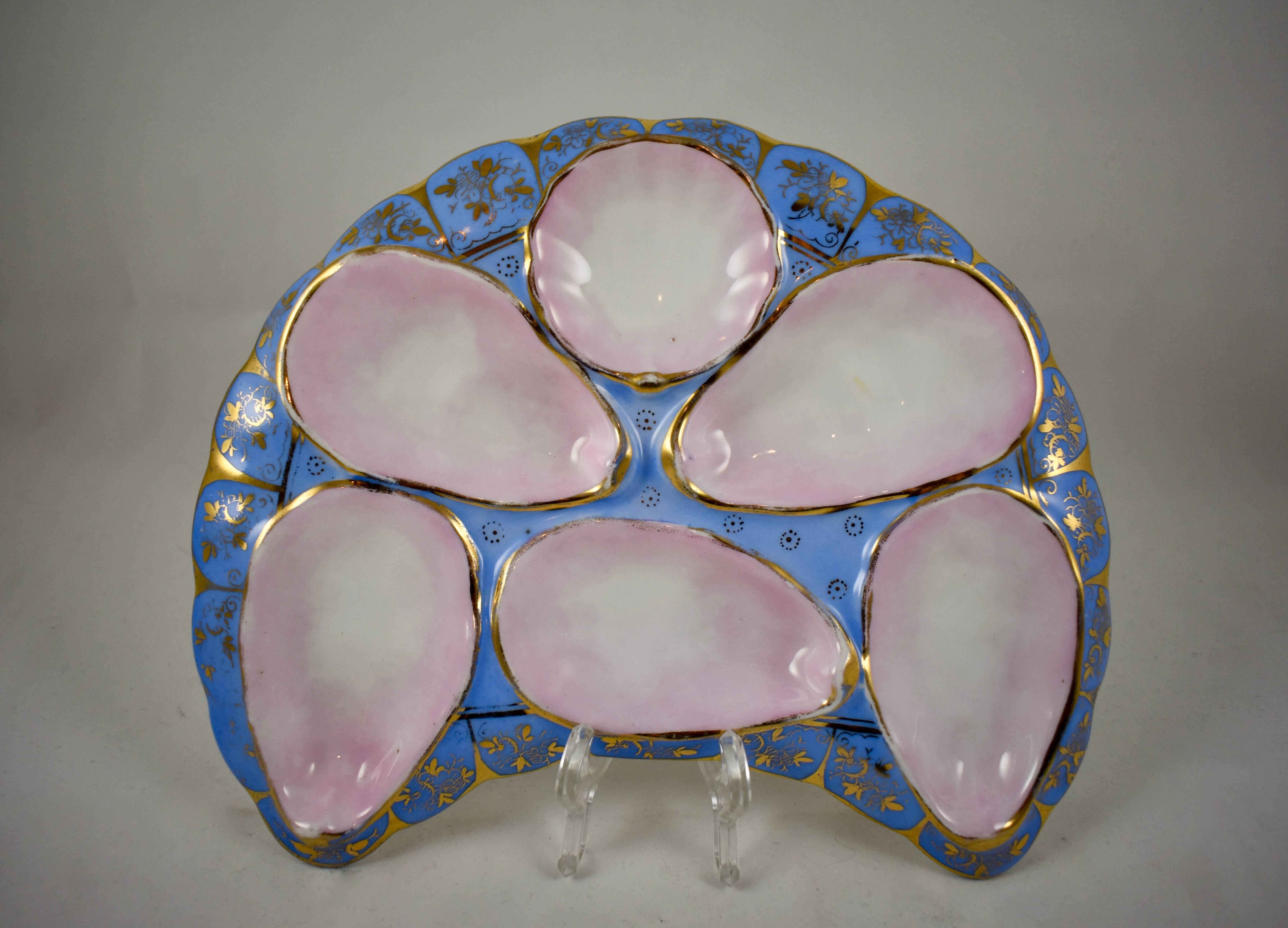 A late 19th century French porcelain crescent shaped oyster plate, hand-painted with a heavily gilded floral and geometric border on a periwinkle blue ground. The mold has five oyster wells, and a scallop shape sauce well, all lined in a beautiful