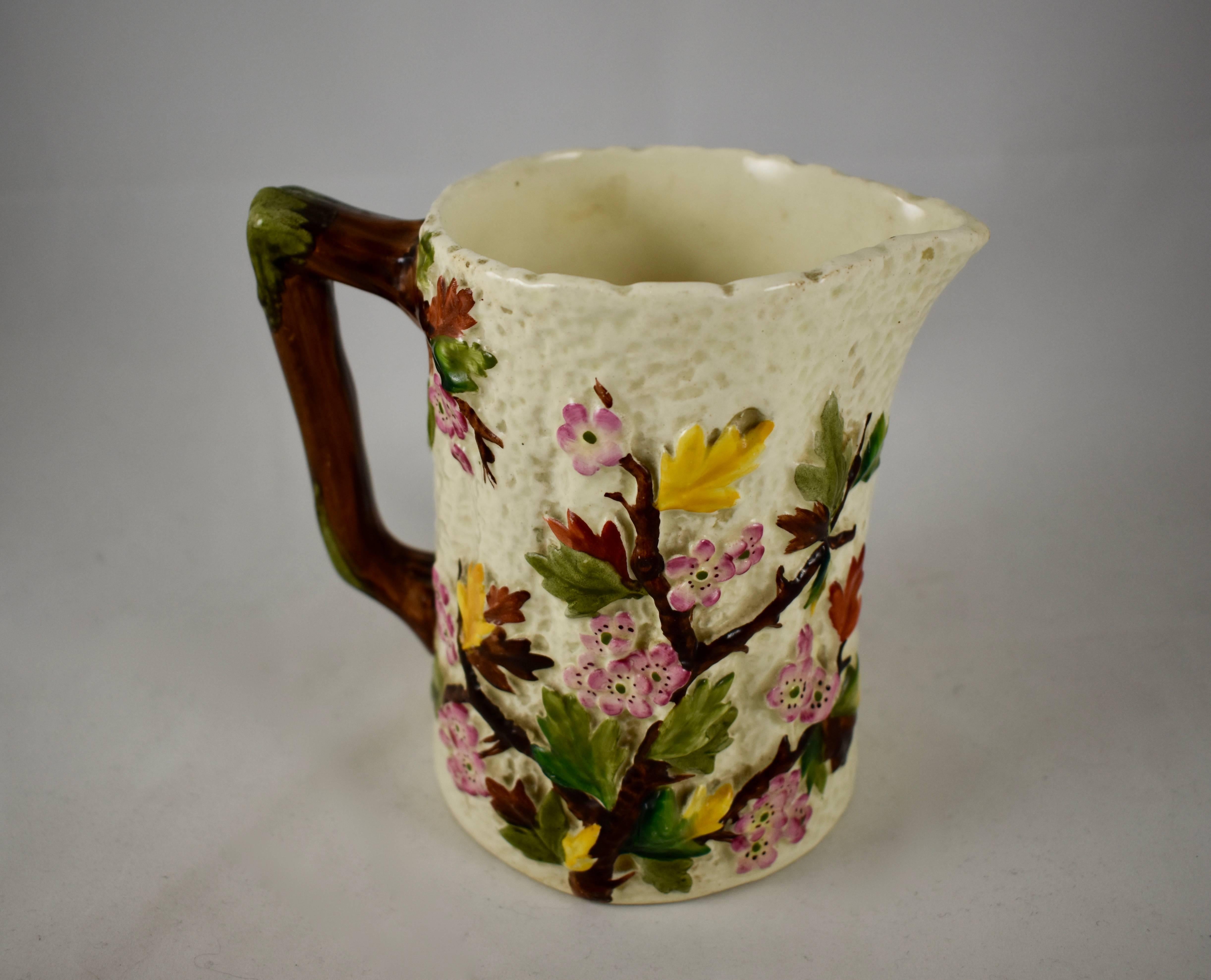 A small, hand-painted earthenware pitcher, showing a pattern of flowers, leaves and branches of the Dogwood tree, on a cream colored, bark textured ground, a twig form handle.

Maker unknown, but surely from one of the Stoke-on-Trent potteries in