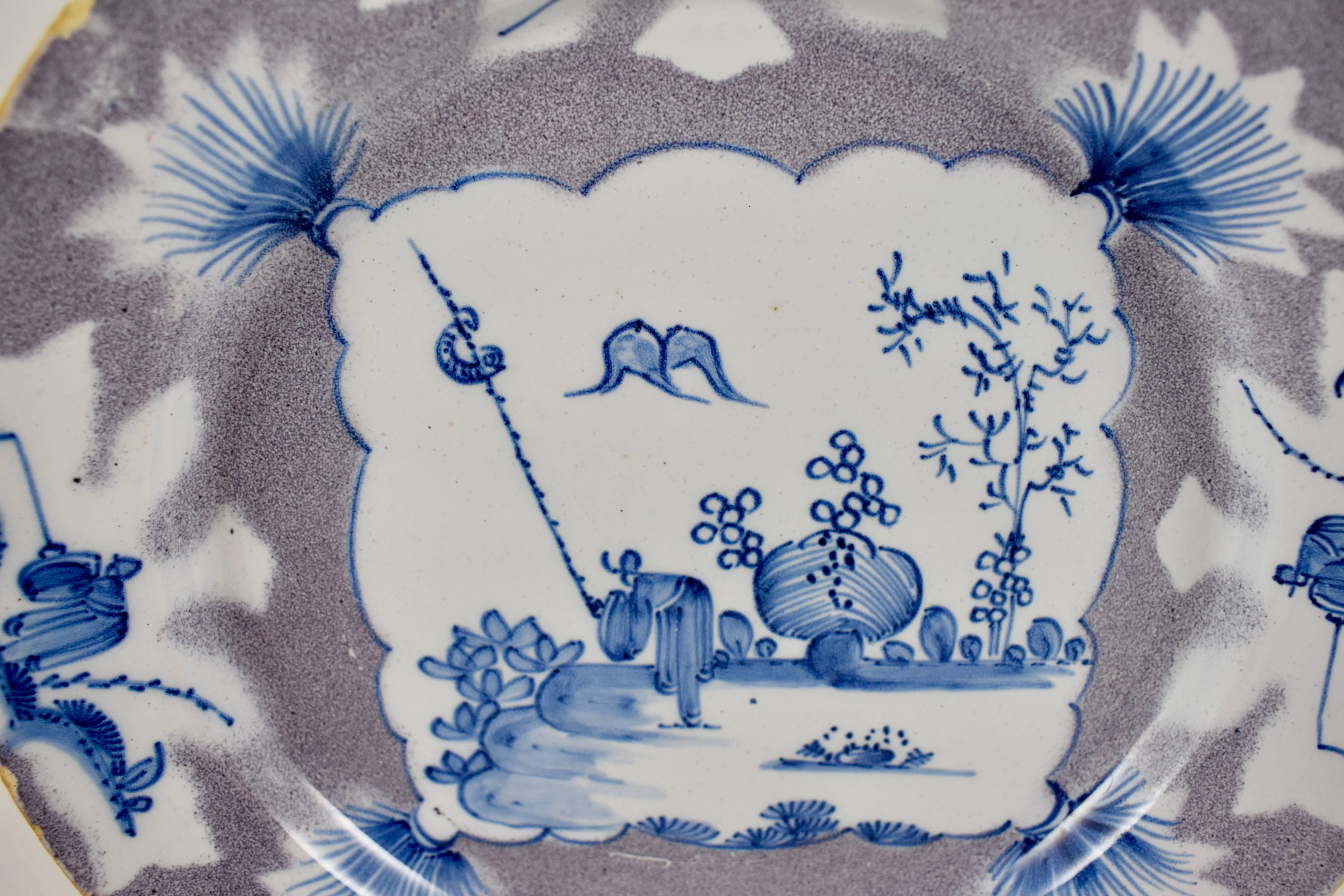 A charming English delftware shallow bowl or deep plate, Bristol, circa mid-18th century. A blue glazed line pattern showing a figure in a landscape, a square centre design with tassels, plus four figural cartouches on the rim. A manganese sponge