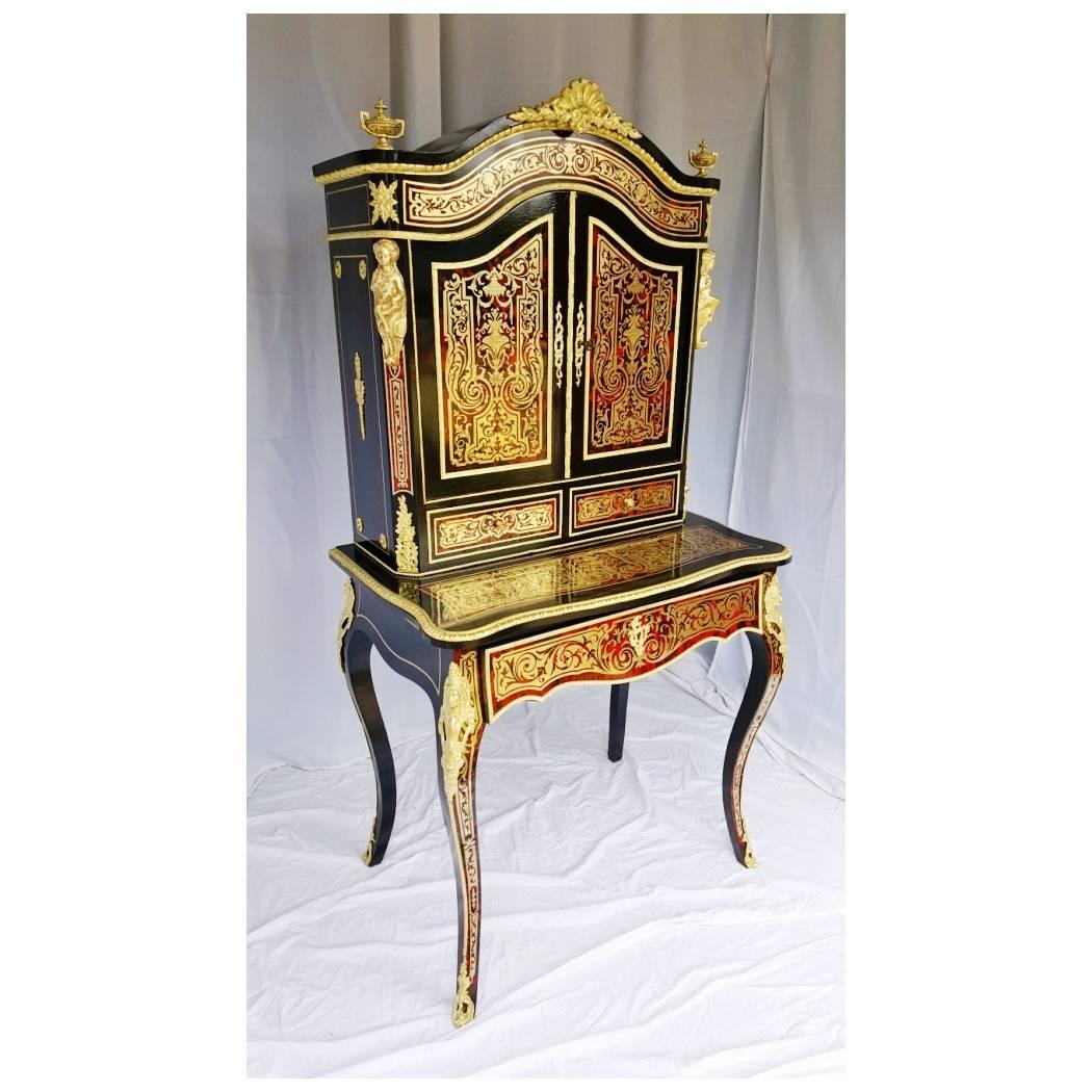 Boulle marquetry of tortoiseshell and brass. Important ornamentation with gilded bronze caryatids, falls, multiple molds, shoes, torches, spinning tops. Drawer with sliding tray including a writing table. Inside the upper part we find mahogany
