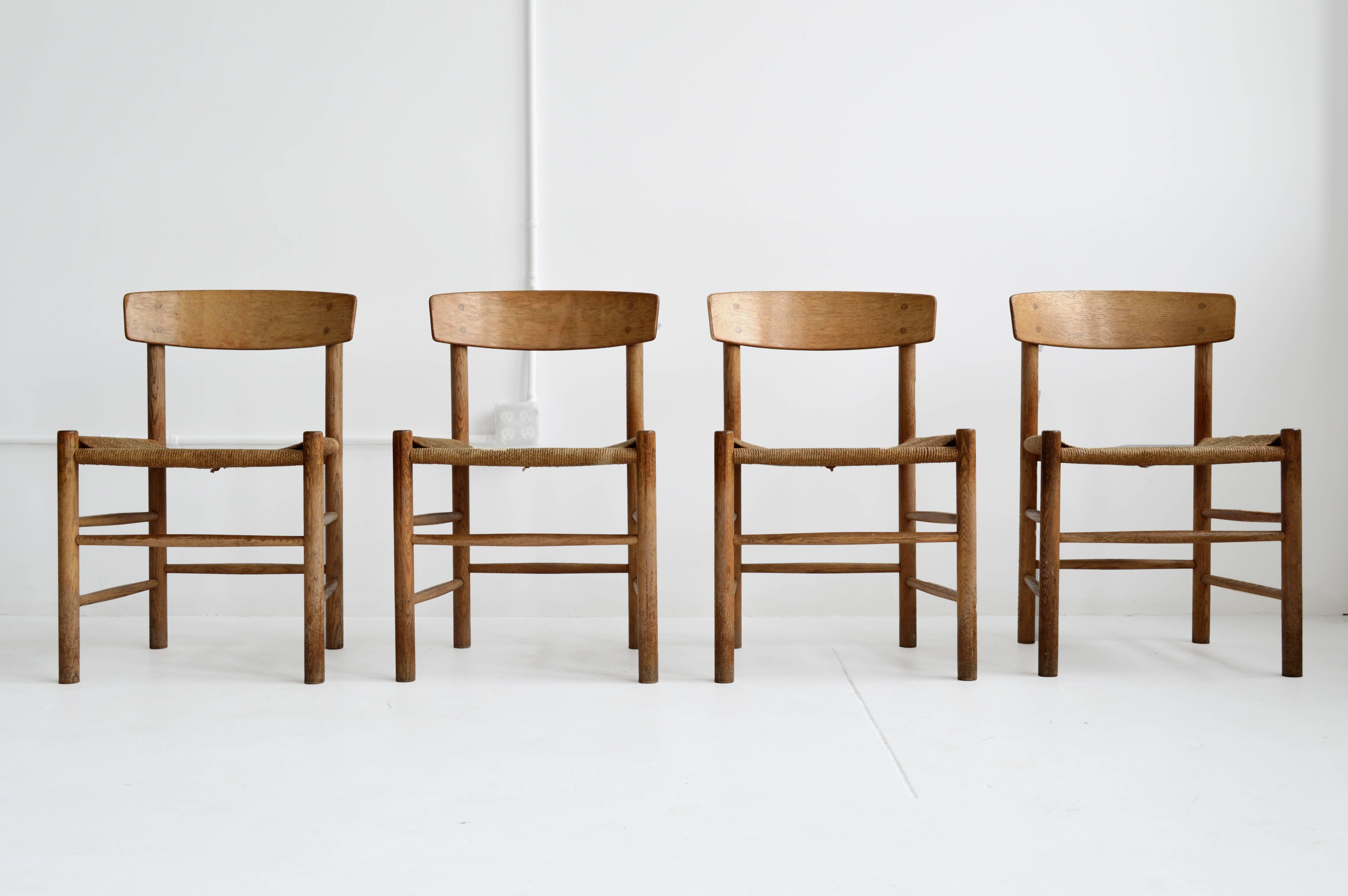 Four solid oak and rush dining chairs by Danish furniture designer Børge Mogensen. The curved wood seat back and woven rush seats provide a comfortable, yet chic set of Scandinavian modern dining chairs. Set of four in good vintage condition with