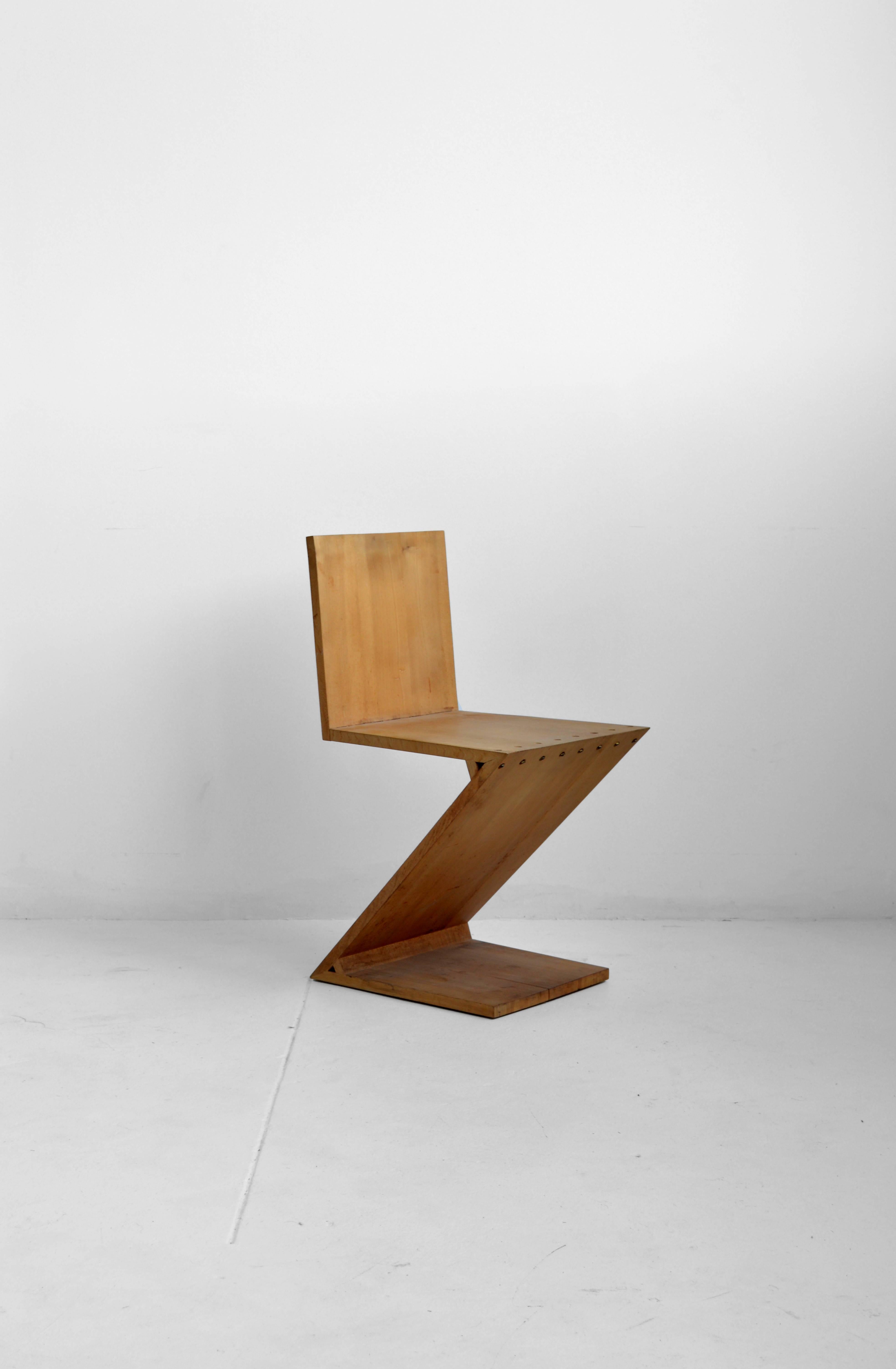 Iconic riveted Zig-Zag chair by Dutch furniture designer and architect Gerrit Thomas Rietveld and produced by Gerard van de Groenekan. Striking Silhouette of solid elm with brass rivets. Signed with branded manufacturer's mark to underside.