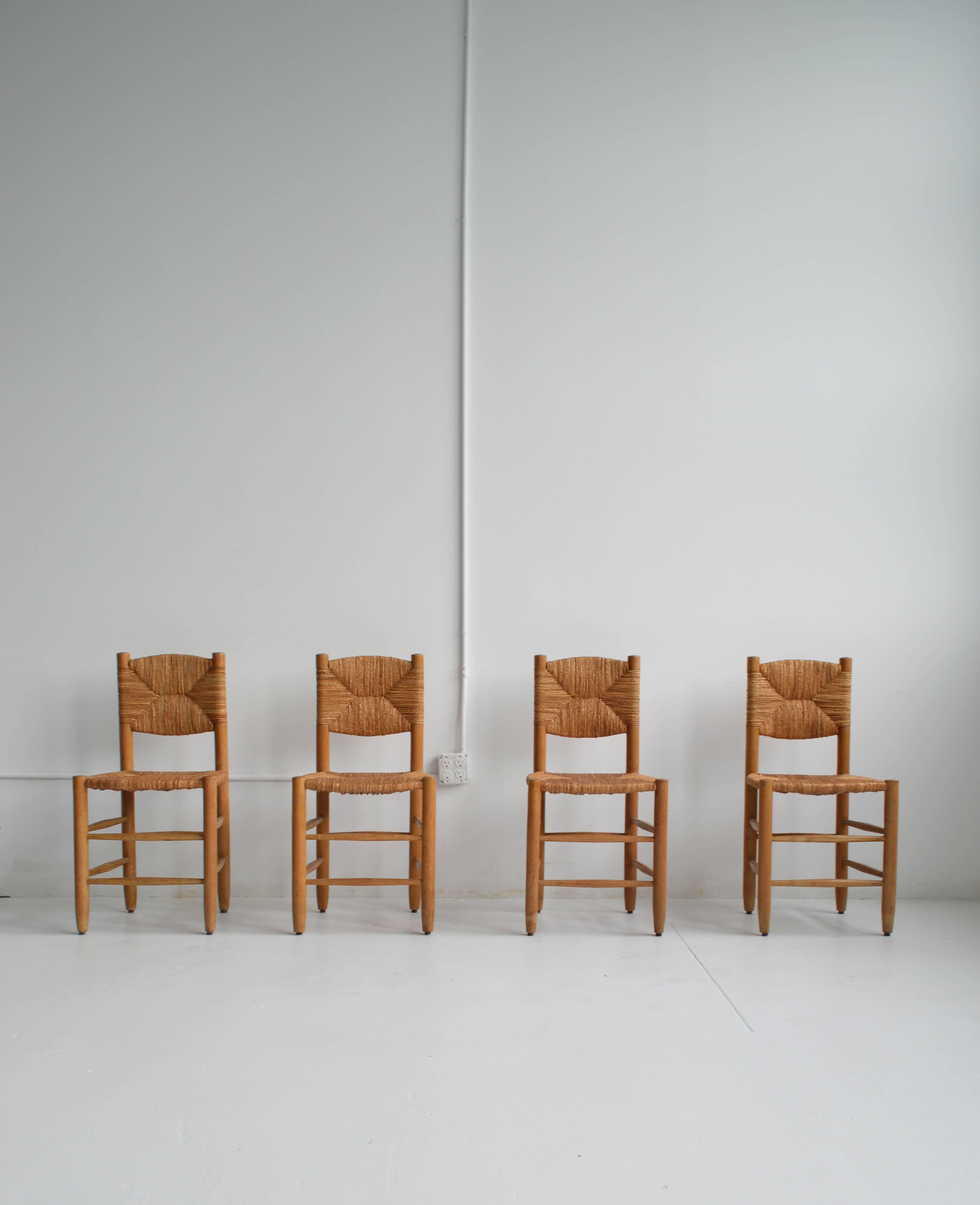 Set of four solid ashwood and rush straight-backed dining chairs by iconic French modern designer, Charlotte Perriand. These chairs achieve a striking balance of relaxed and refined design. The set is in good vintage condition with a beautiful