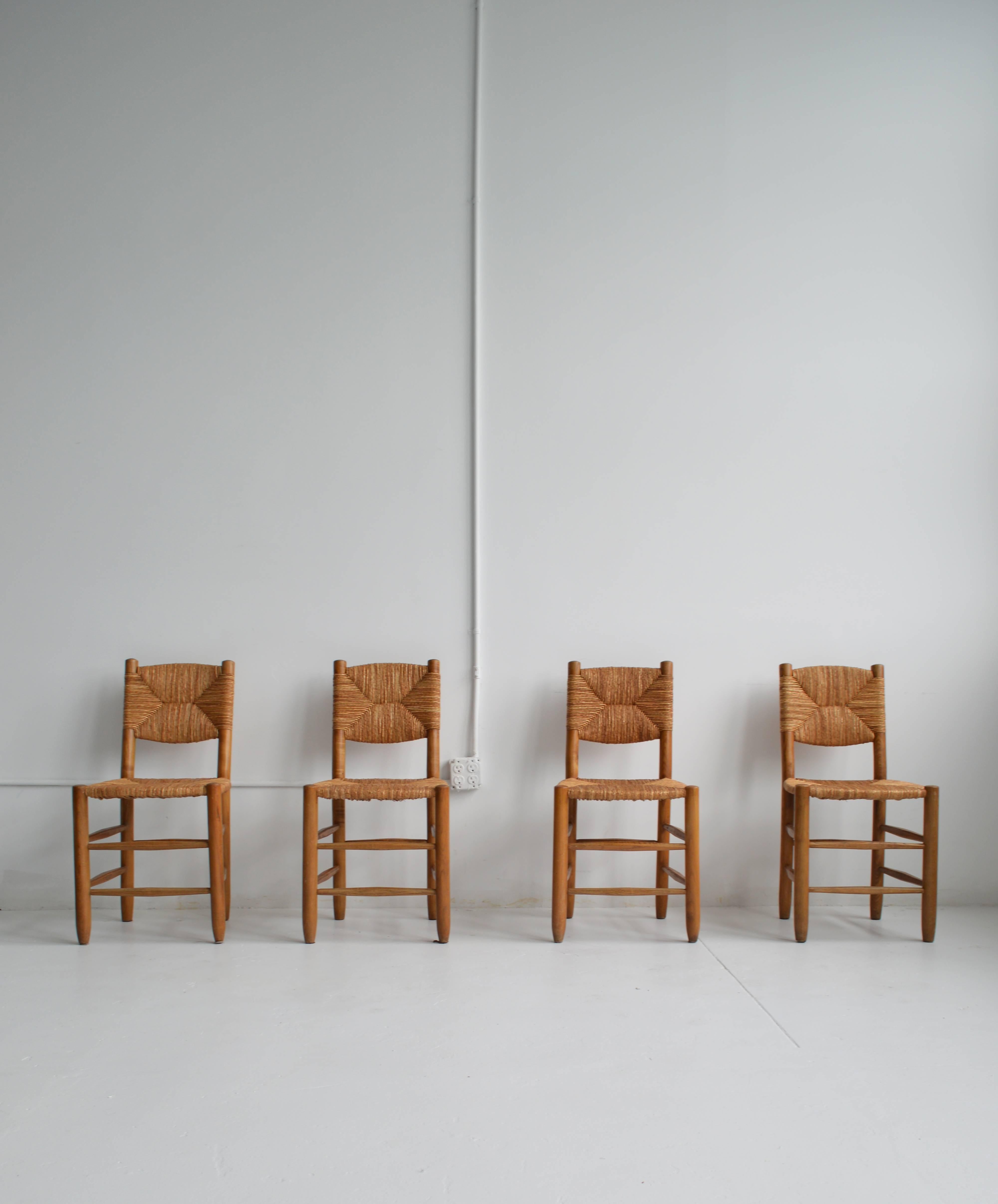 Set of four solid ash wood and rush angled-backed dining chairs by iconic French Modern designer, Charlotte Perriand. These chairs achieve a striking balance of relaxed and refined design. The set is in good vintage condition with a beautiful patina