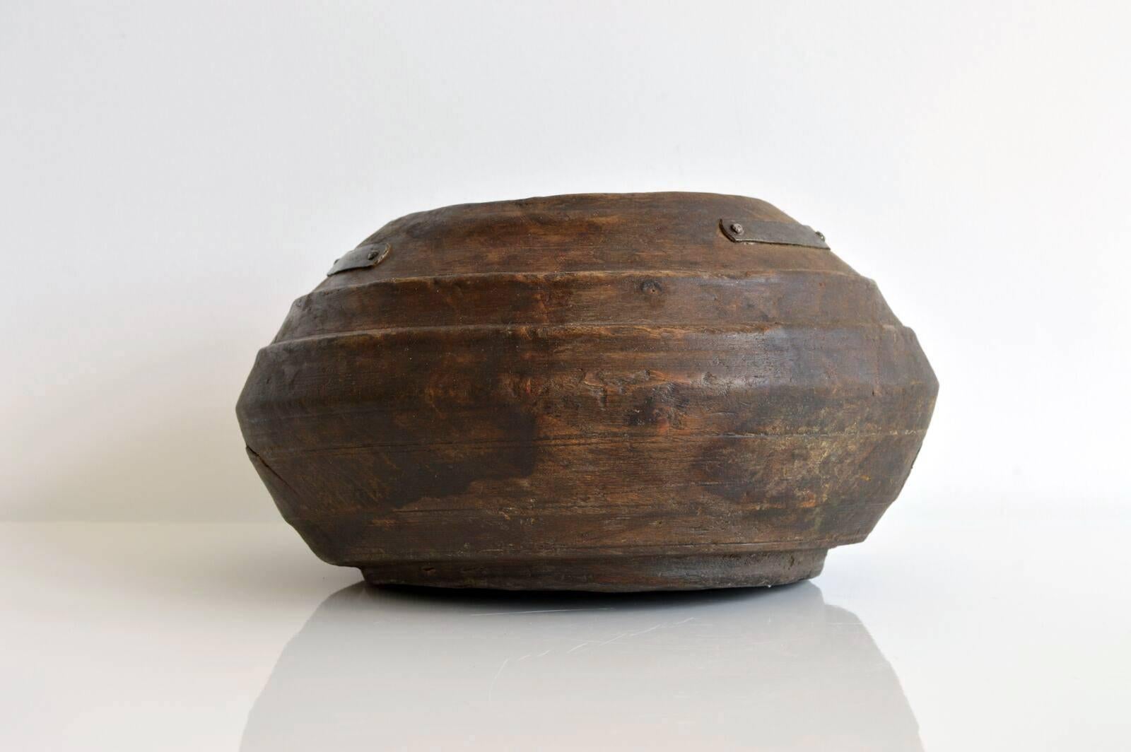 Rustic carved wood vessel by an unknown artisan, originally from Iran. The bowl has a beautiful patina finish with metal hardware detail on either side of the top of the bowl's exterior. This piece would make a great natural decorative object,