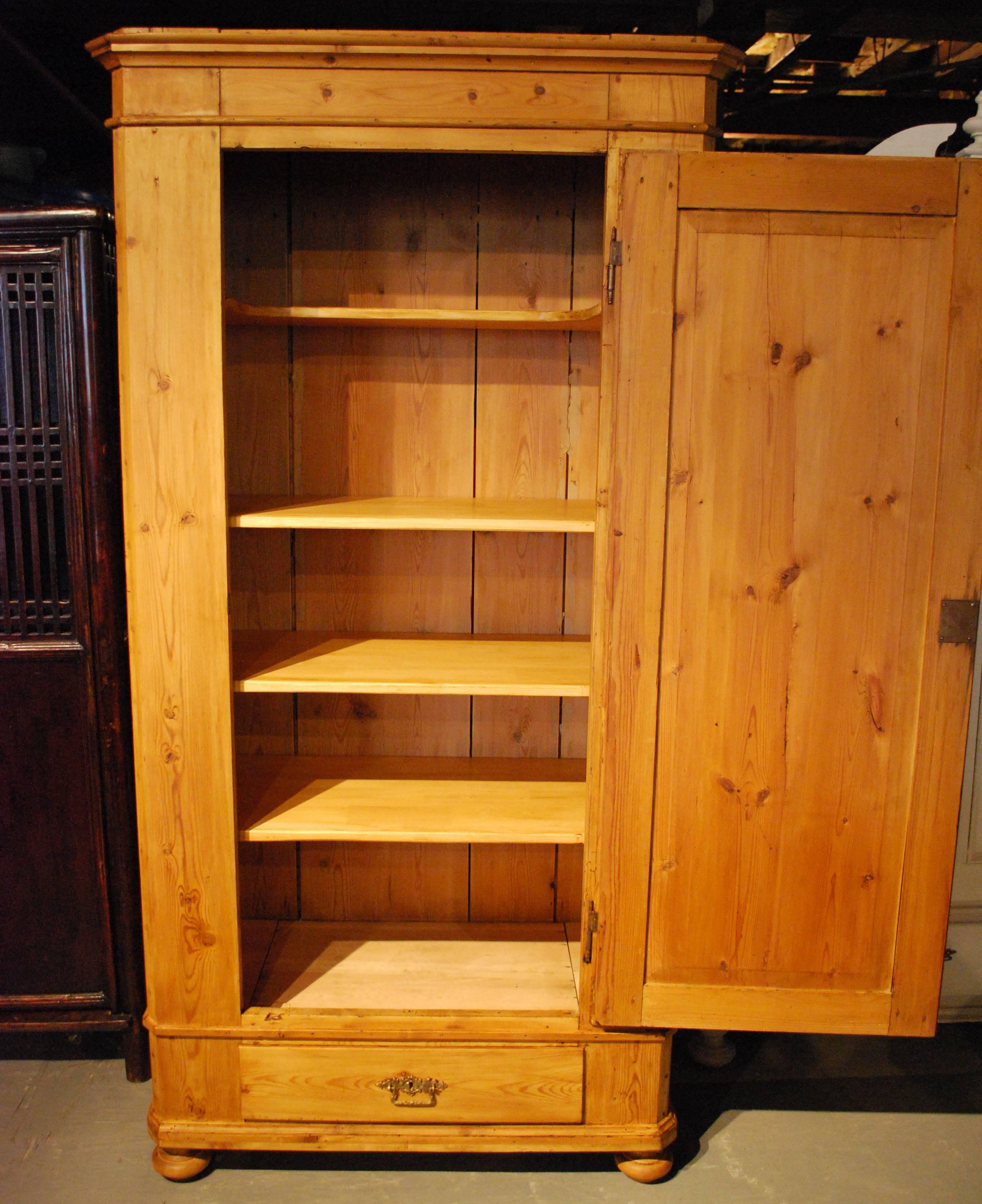 An antique Danish pine armoire displaying a nicely molded top, canted edges and an arched top recessed panel door that opens to a shelved interior with two secret compartments. The armoire shows a dovetailed base drawer, bun and block feet, and a