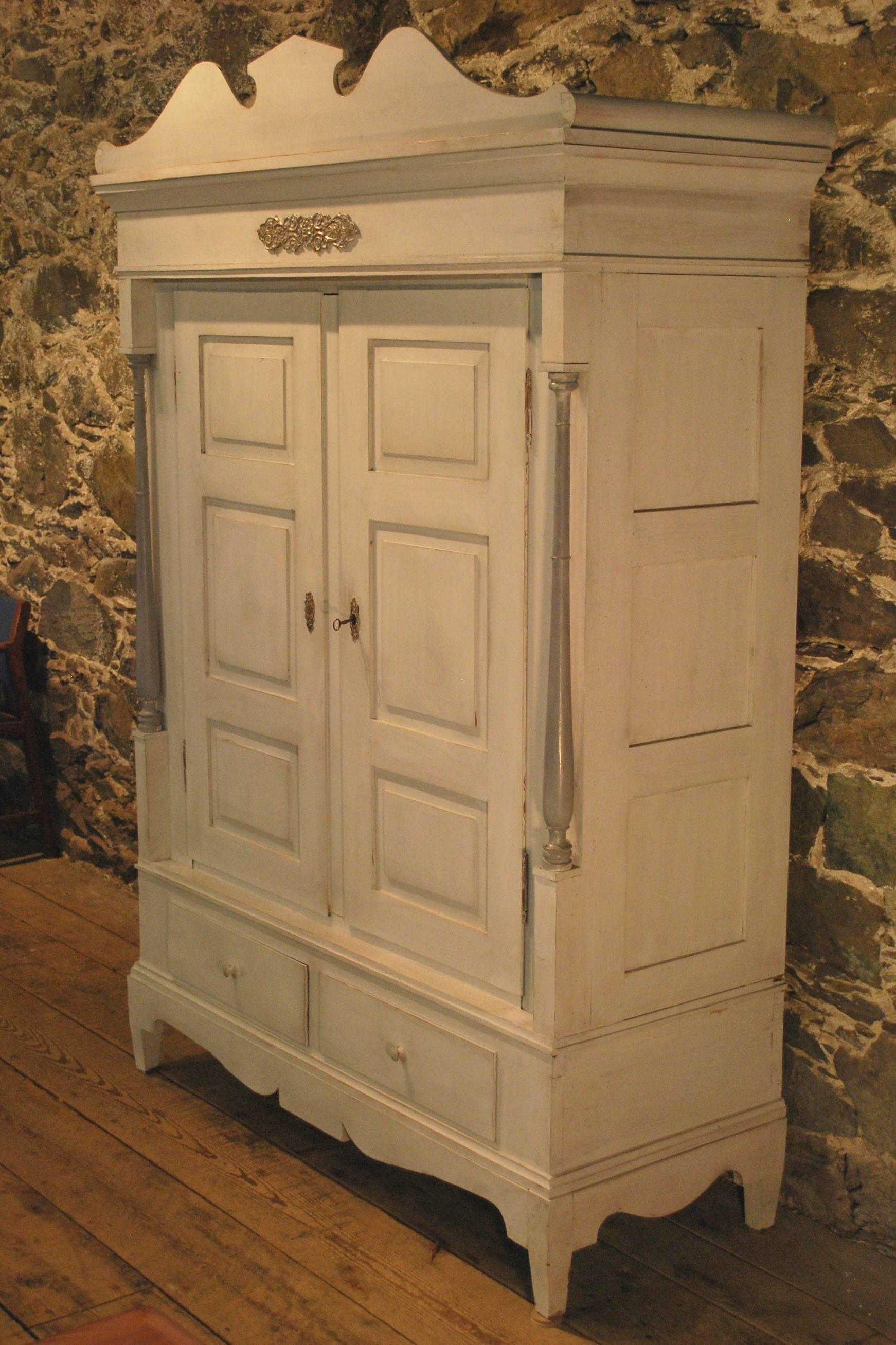 Antique armoire with Gustavian style paint. This armoire has a removable pediment top over two set-back raised paneled doors, flanked by full turned columns. The recessed side panels and the curved skirt add a subtle balance to the cabinet. While