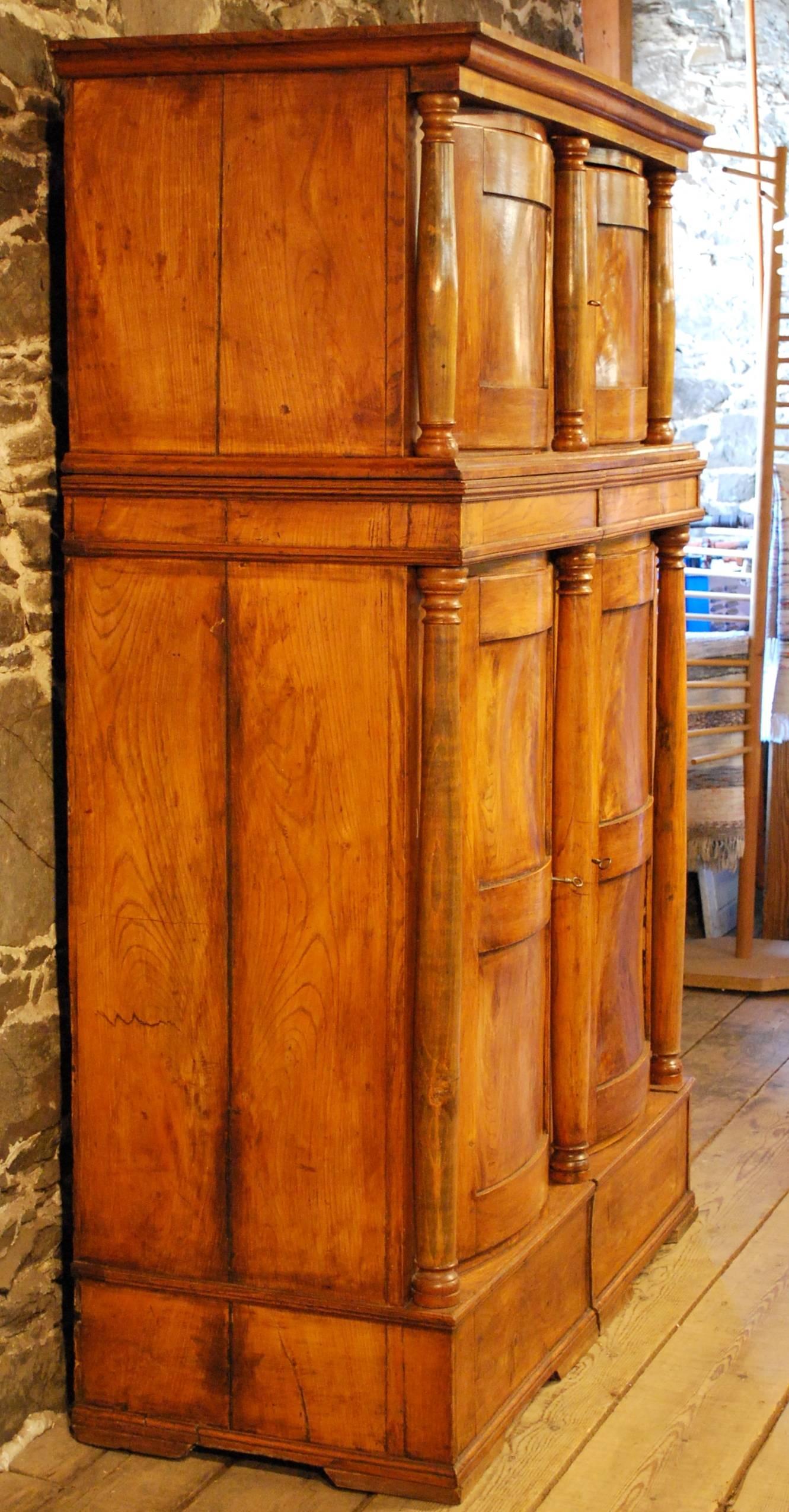 A striking antique Danish elmwood four door hat cabinet featuring a two-tiered bow Front design with impressive architectural details and a roomy interior: beautiful elegant storage or closet which could be in a public room. Transports in three