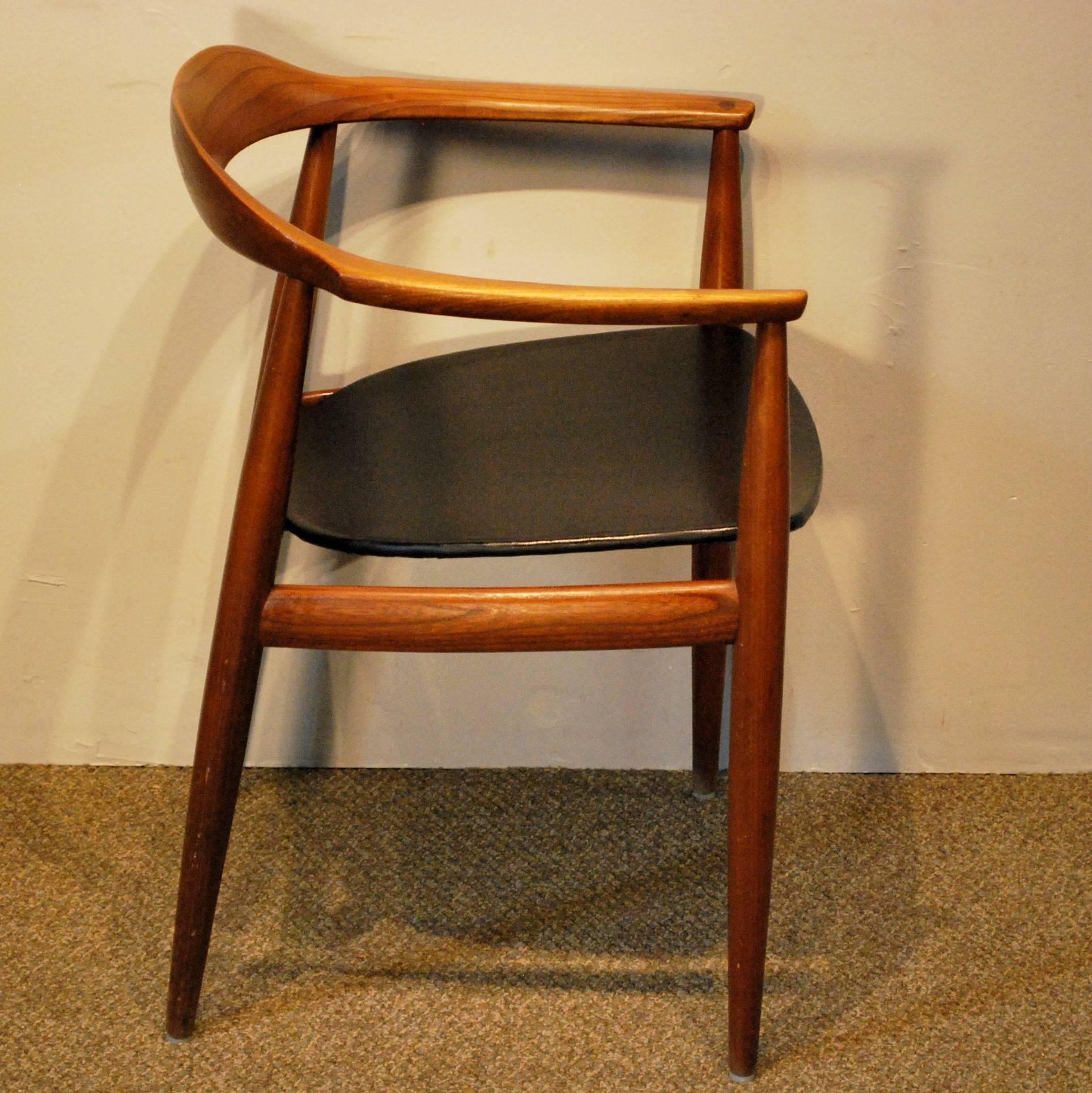 A larger than normal Mid-Century Modern teak/leather armchair displaying a single piece of steam bent solid teak for the backrest and armrests with a black leather upholstered seat on a curved teak frame in the manner of Hans Wegner's Model 503,