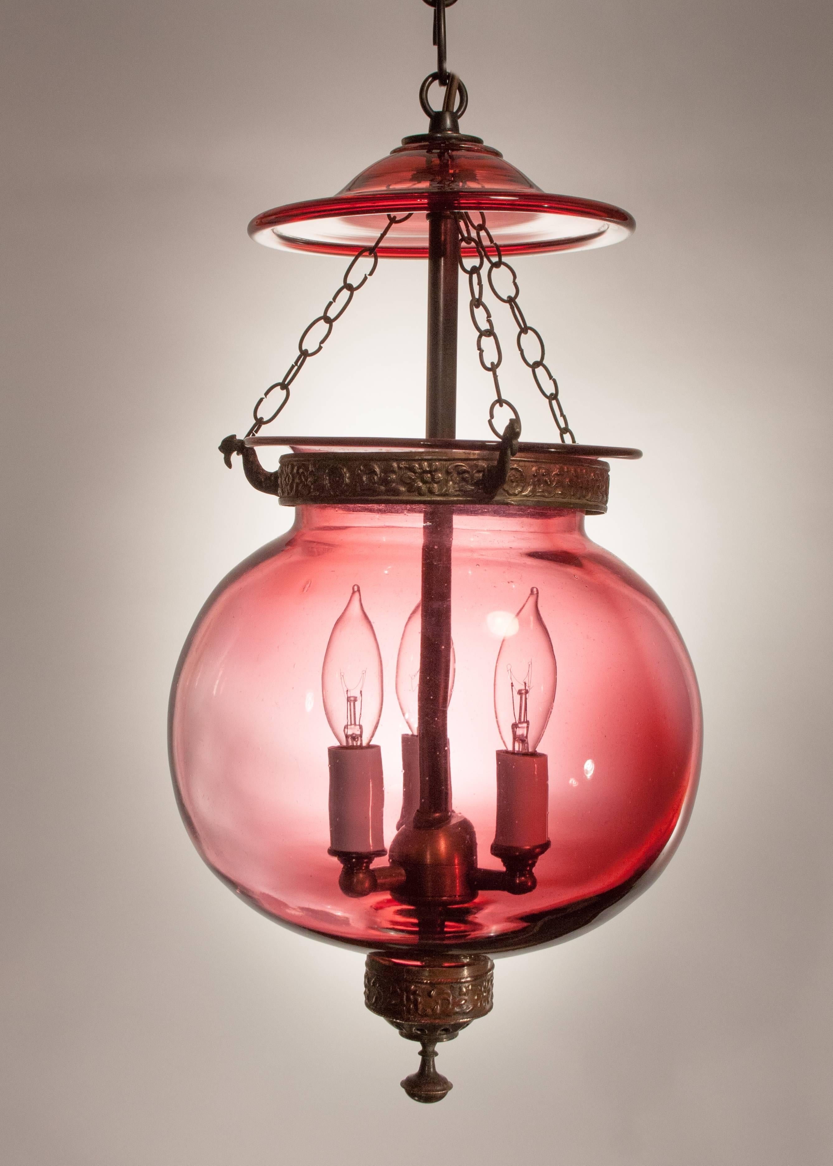 Cranberry red globe bell jar lantern, circa 1860, with lovely form and tonal gradations consistent with the quality and age of the hand blown glass. This English hall lantern has its original smoke bell, as well as decorative brass band and finial.