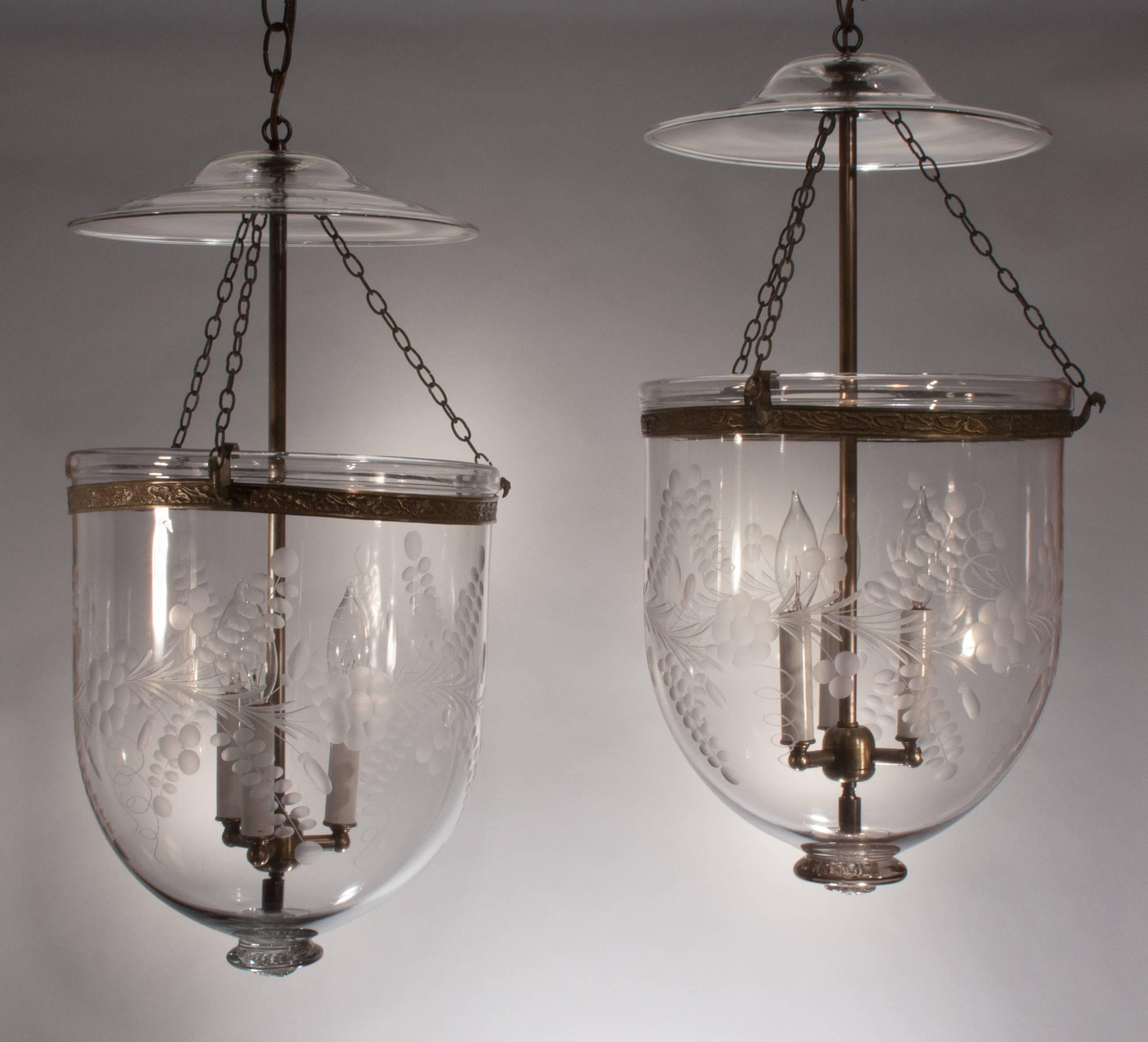 Pair of large English bell jar hall lanterns, circa 1880, with etched floral and vine design. These handblown glass pendants have their original smoke bells and decorative brass bands. The bell jars are newly electrified, each with a three-bulb