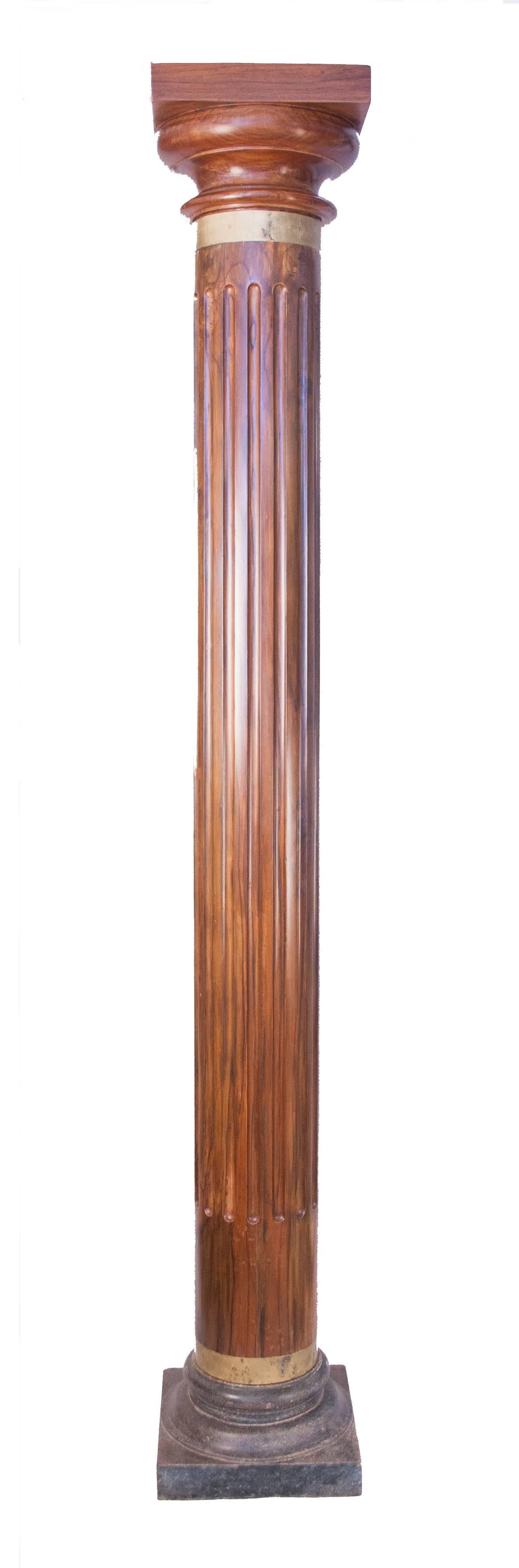 A handsome pair of reeded columns from British India in richly finished teak, circa 1920. The round wooden shafts of these pillars are hand-gadrooned and finished with original brass collars. The columns rest on square, solid granite bases and are