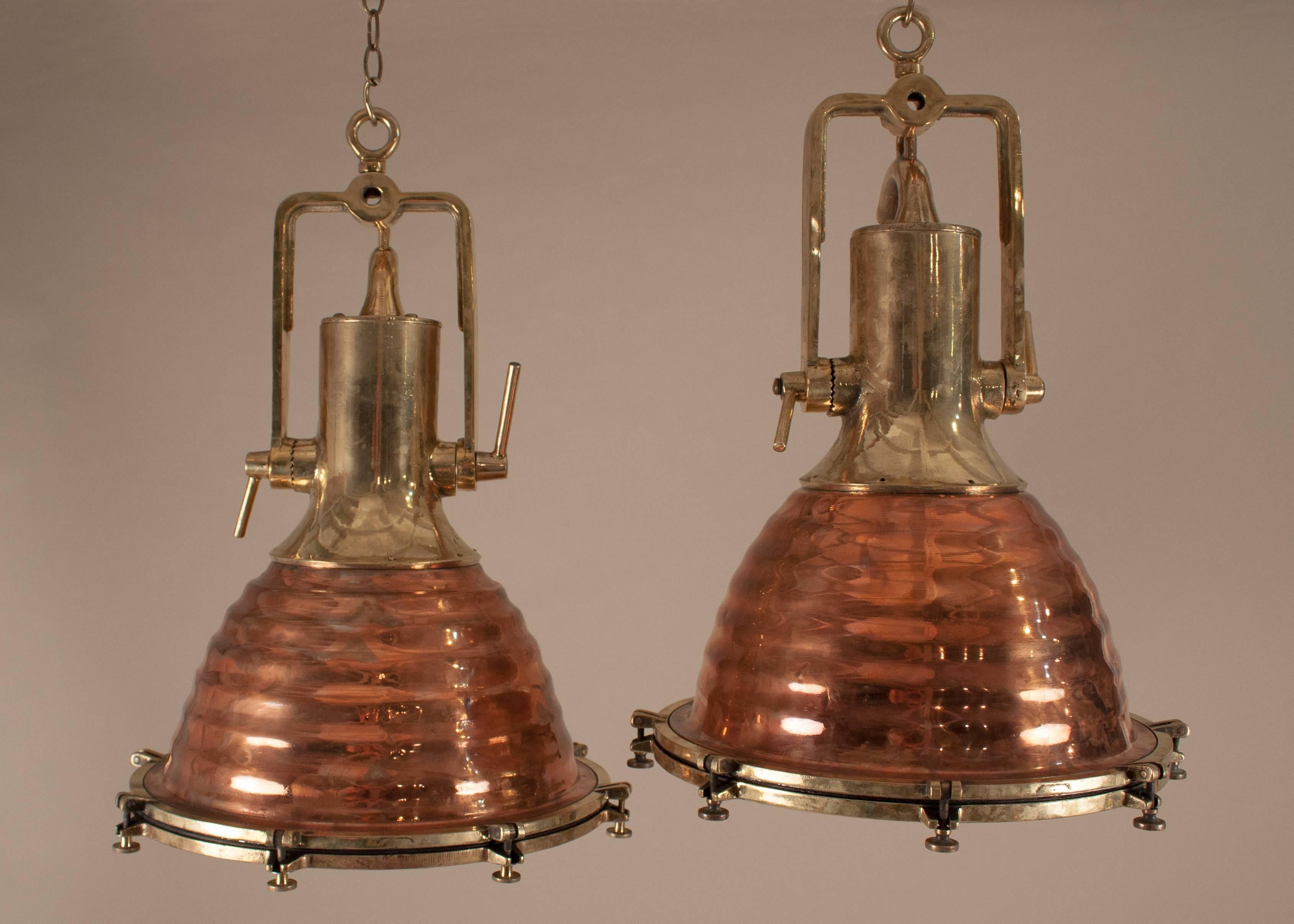 An authentic pair of large polished copper and brass ship's deck or cargo spotlights with fluted exteriors, copper interiors and tempered glass lenses. Salvaged from a maritime vessel, these mid-century nautical pendants have wonderful form and