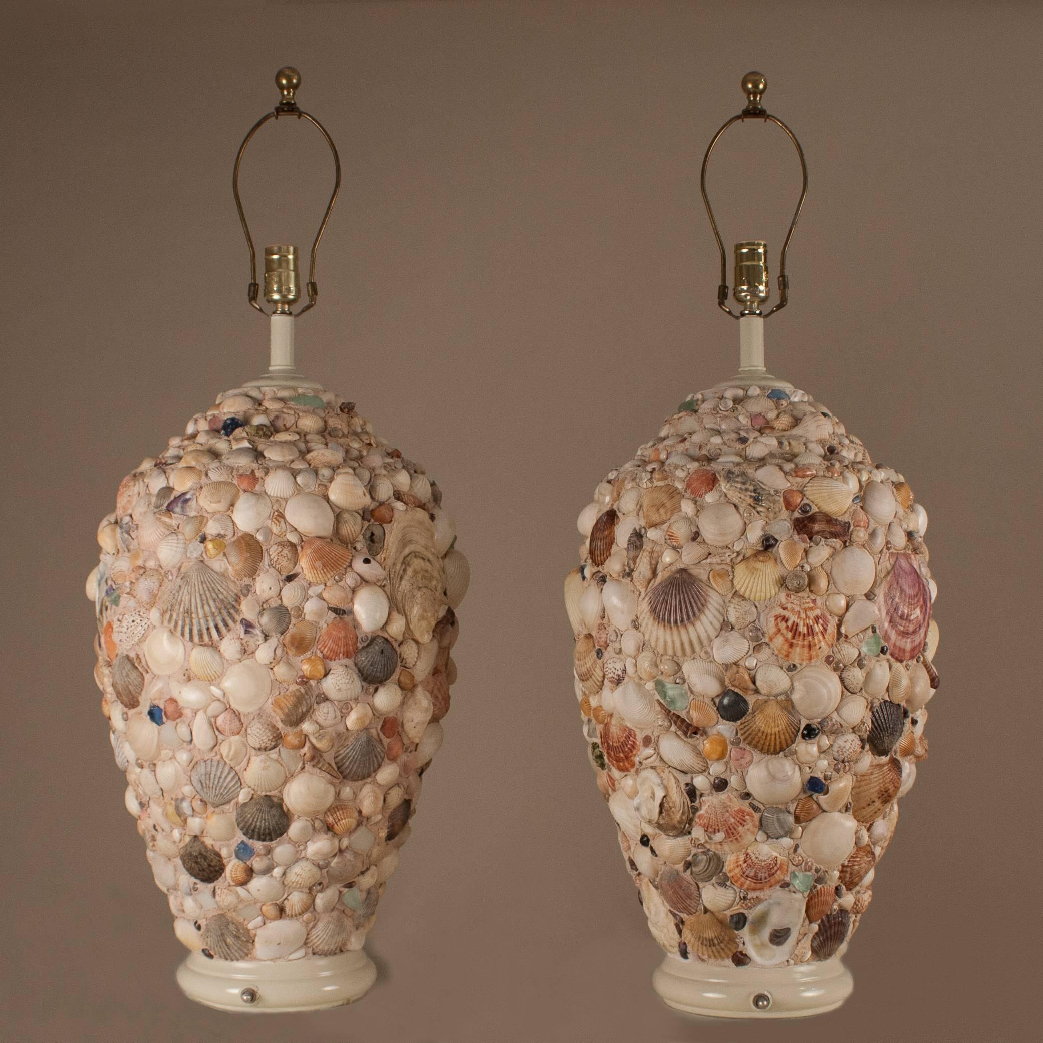 A pleasing palette of seashells and green and blue sea glass adorn these positively coastal 1960s table lamps. The lamps stand tall at 27.5 inches from the painted wooden base to socket top, 34 inches to the top of the brass finial. The diameter (at
