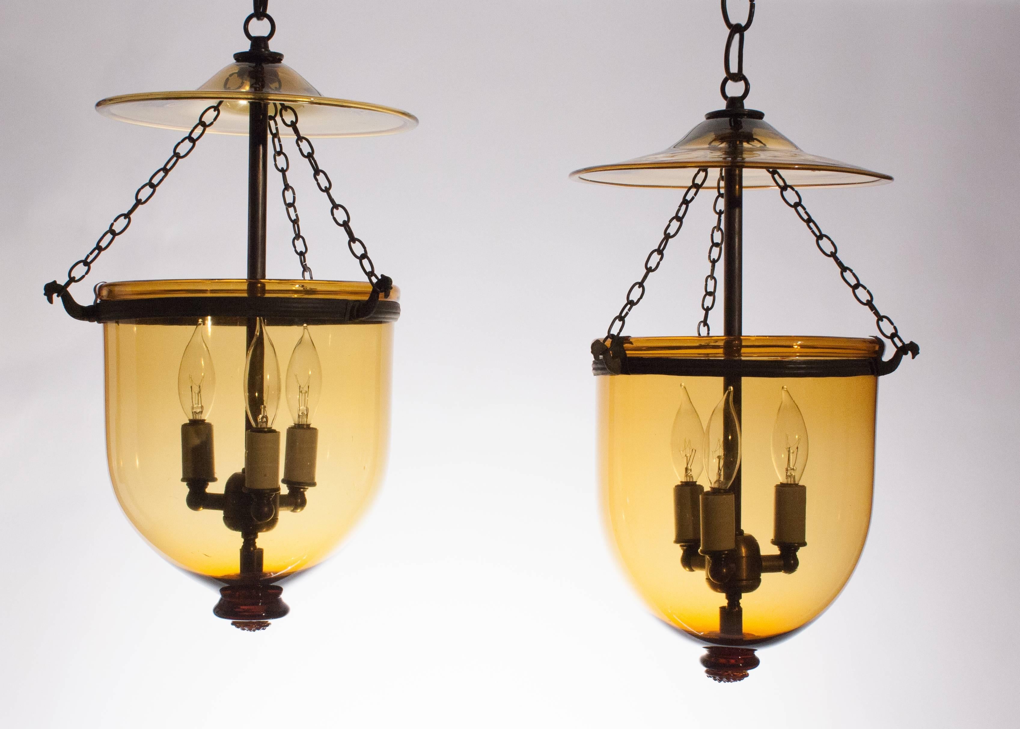 An exceptional pair of 19th century amber colored glass bell jar lanterns. These English hall lanterns emanate a warm, honeyed hue. A sprinkling of small air bubbles speak to the quality and age of the handblown glass. The bell jars are in excellent