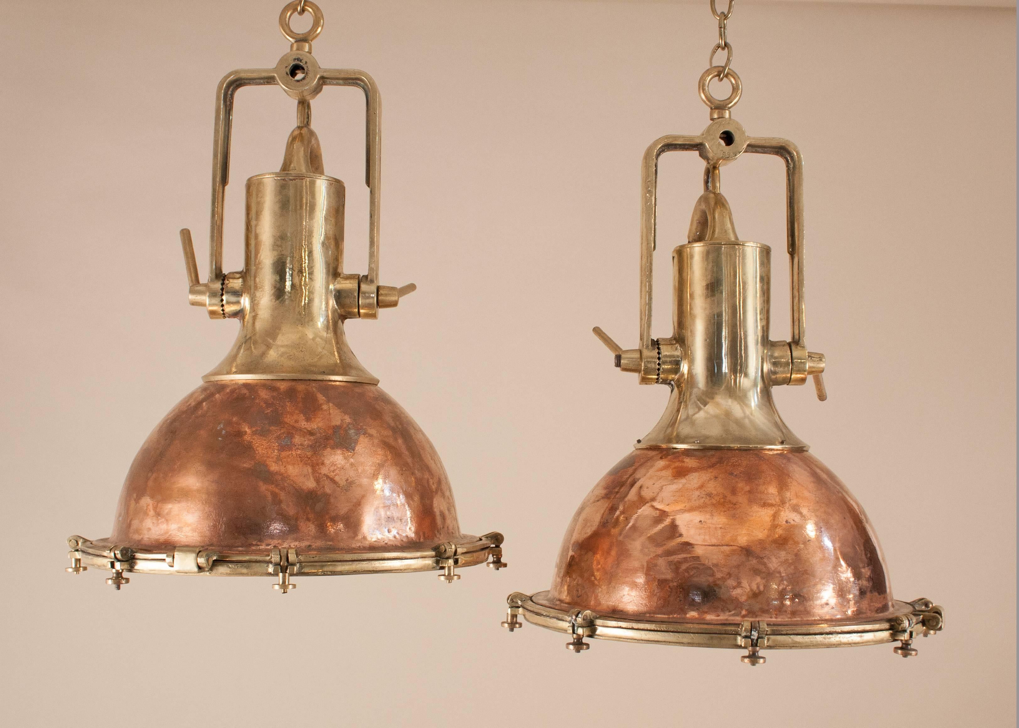An authentic pair of large 1950s copper and brass ship's deck lights with superb form and patina. Salvaged from a maritime vessel and attentively restored to near-original condition, these nautical pendants suspend from adjustable solid brass