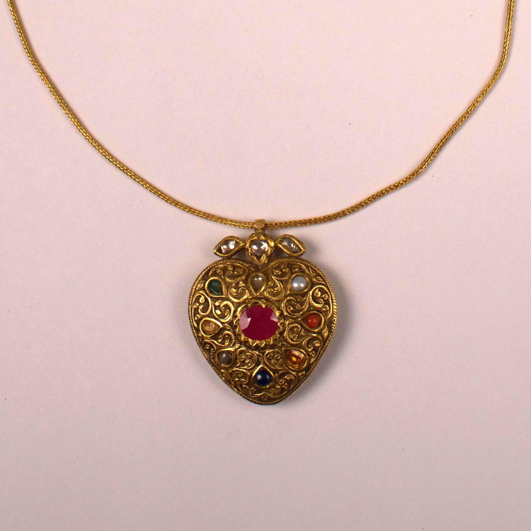 An 18-karat gold heart-shaped Navaratna necklace with nine gemstones representing the planets. Adorned with a tooled floral design on front and back, this traditional pendant from Rajasthan, India features (clockwise) a diamond, pearl, coral,