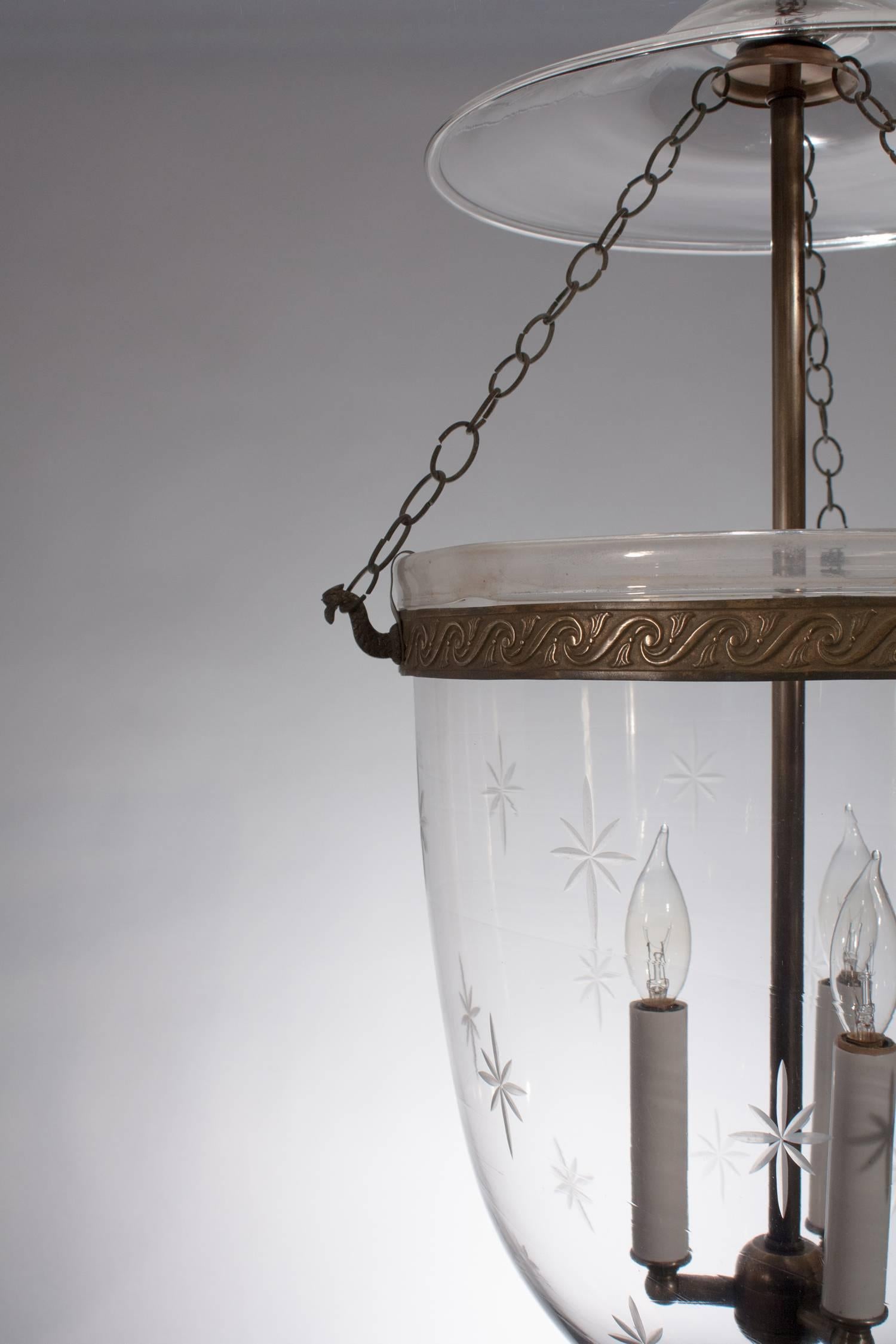 Elegant English hand blown hall lantern, circa 1860, with its original smoke bell, chains and pressed brass band with a flowing tassel design. The bell jar, which has a finely etched star pattern, features desirable air bubbles in the glass and a