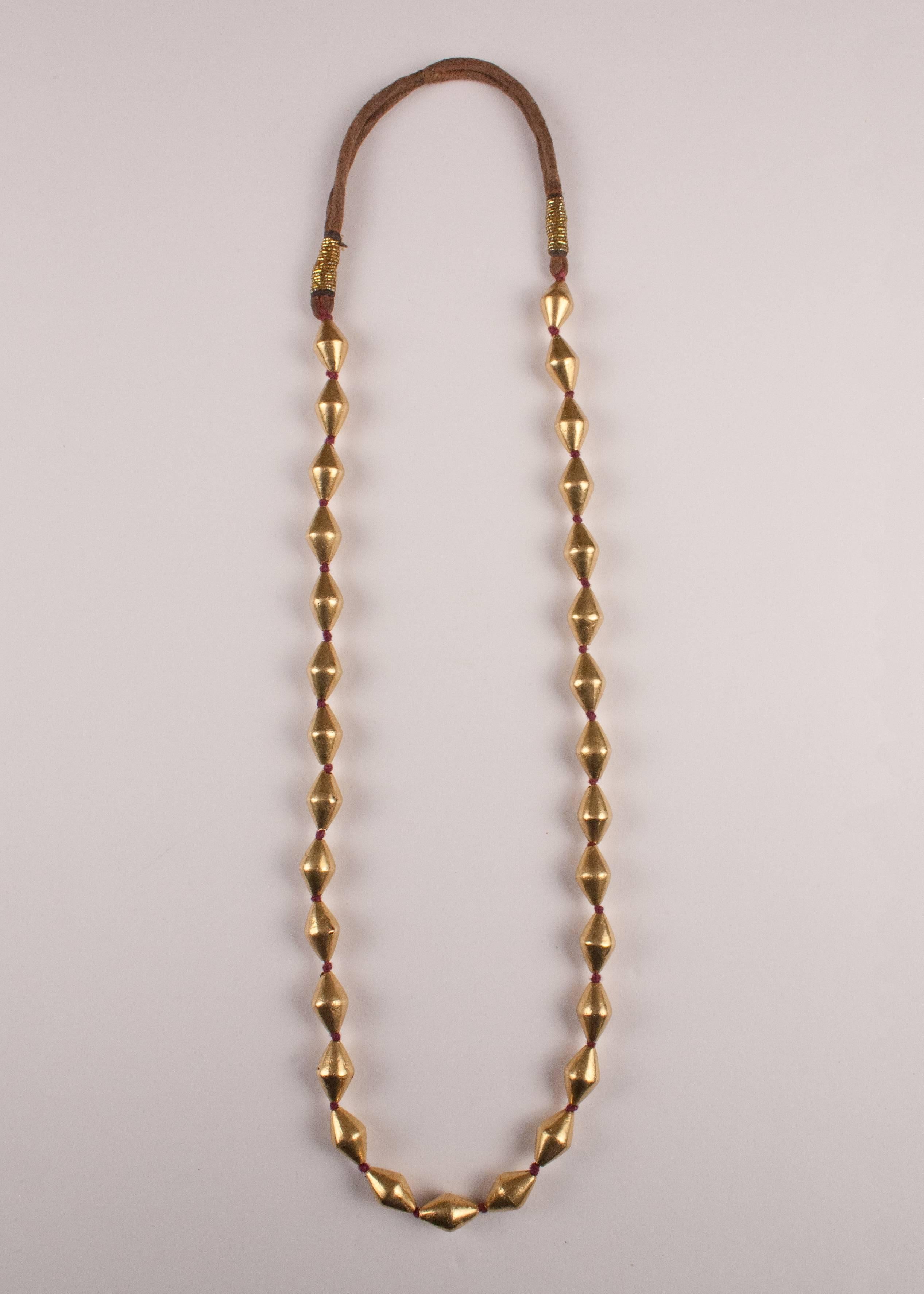 This supple, sensual, traditional strand necklace from India features 30 18-karat gold over wax core beads strung on knotted red-brown cotton thread and finished with a tribal neck cord wrapped with gold thread. Necklace measures: 27 inches length.