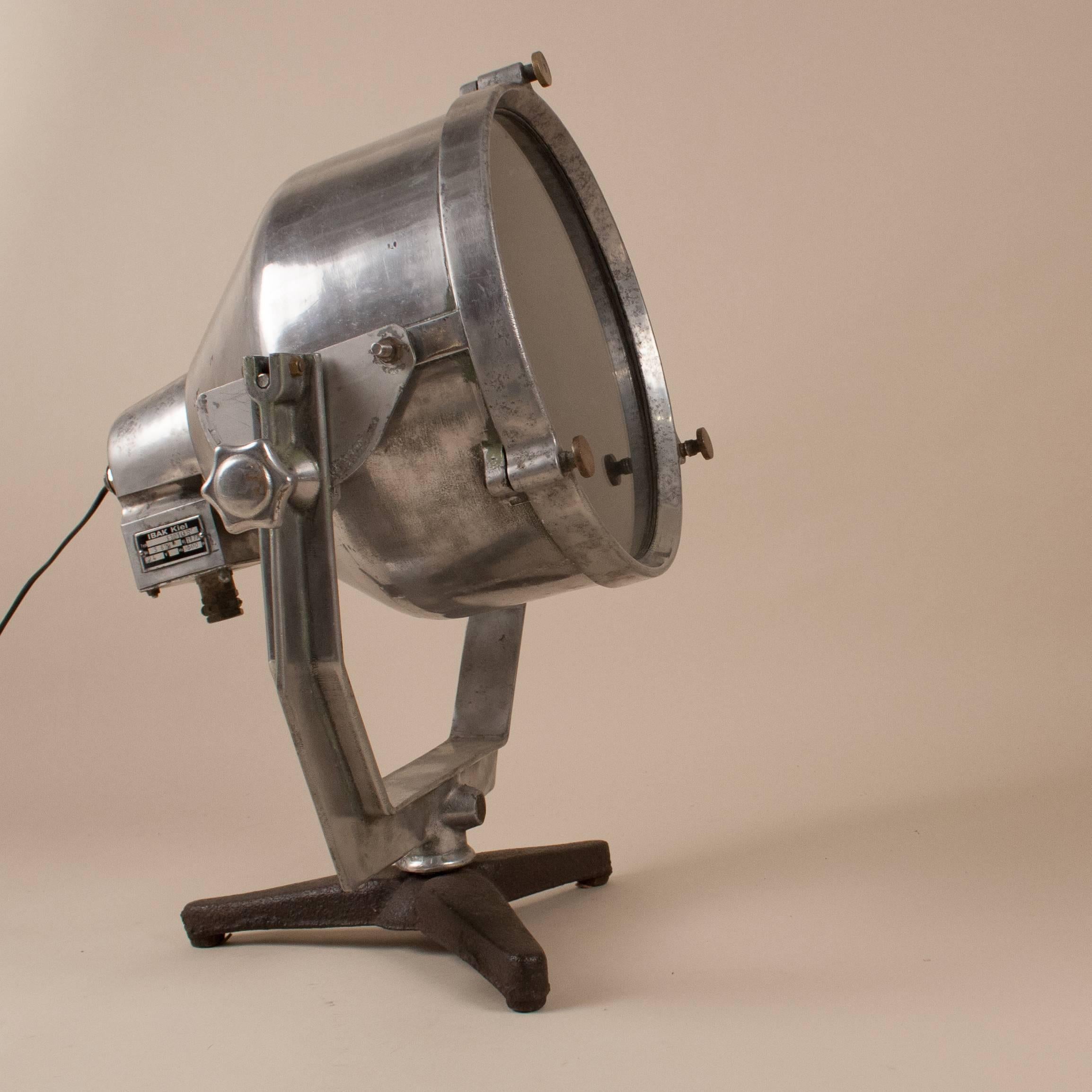 1977 aluminum maritime searchlight from IBAK Kiel of Germany, a leading manufacturer of navigational electronics. The spotlight light is mounted on an adjustable aluminum bracket and stands on a black iron base. It has its original plaque with