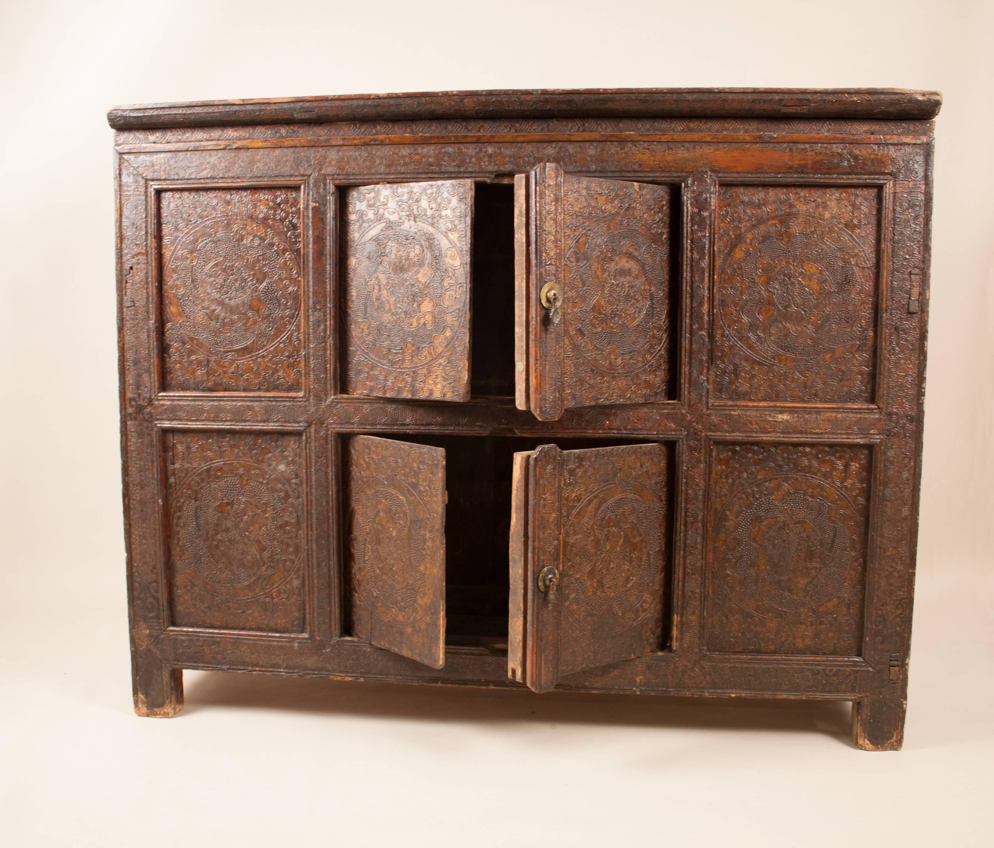 A Tibetan elm cabinet, circa 1920, with original textured paint in muted reddish tones. This Primitive piece features a circular dragon theme on each of the eight panels. The cabinet has mortise and tenon joinery, wooden door hinge pins and