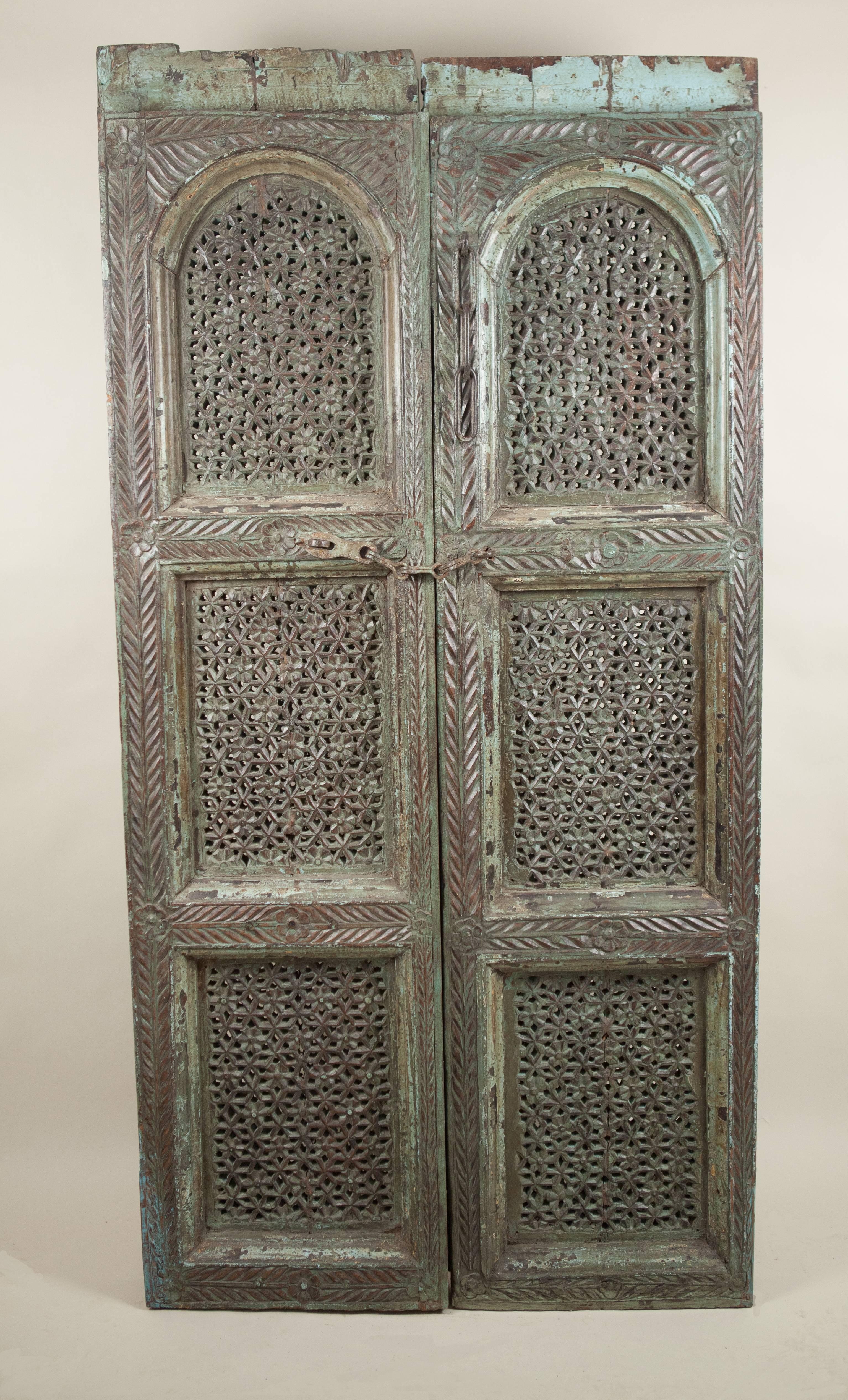 An exceptional pair of intricately hand-carved teakwood doors from India with pierced geometric and floral details. These exotic antique door panels feature original subdued green paint and iron latches.