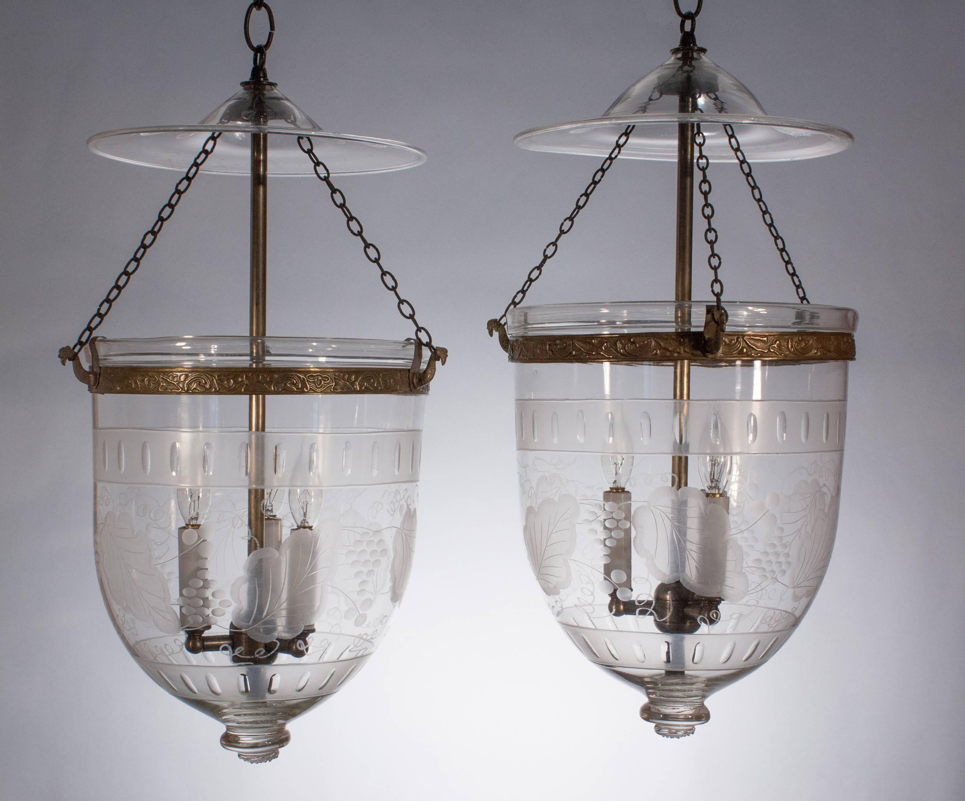An unusual pair of English handblown glass bell jar lanterns with decorative smoke bells, circa 1870. These medium-sized hall lanterns are distinctively decorated with an etched leaf and berry motif bounded by frosted bands at top and bottom. They