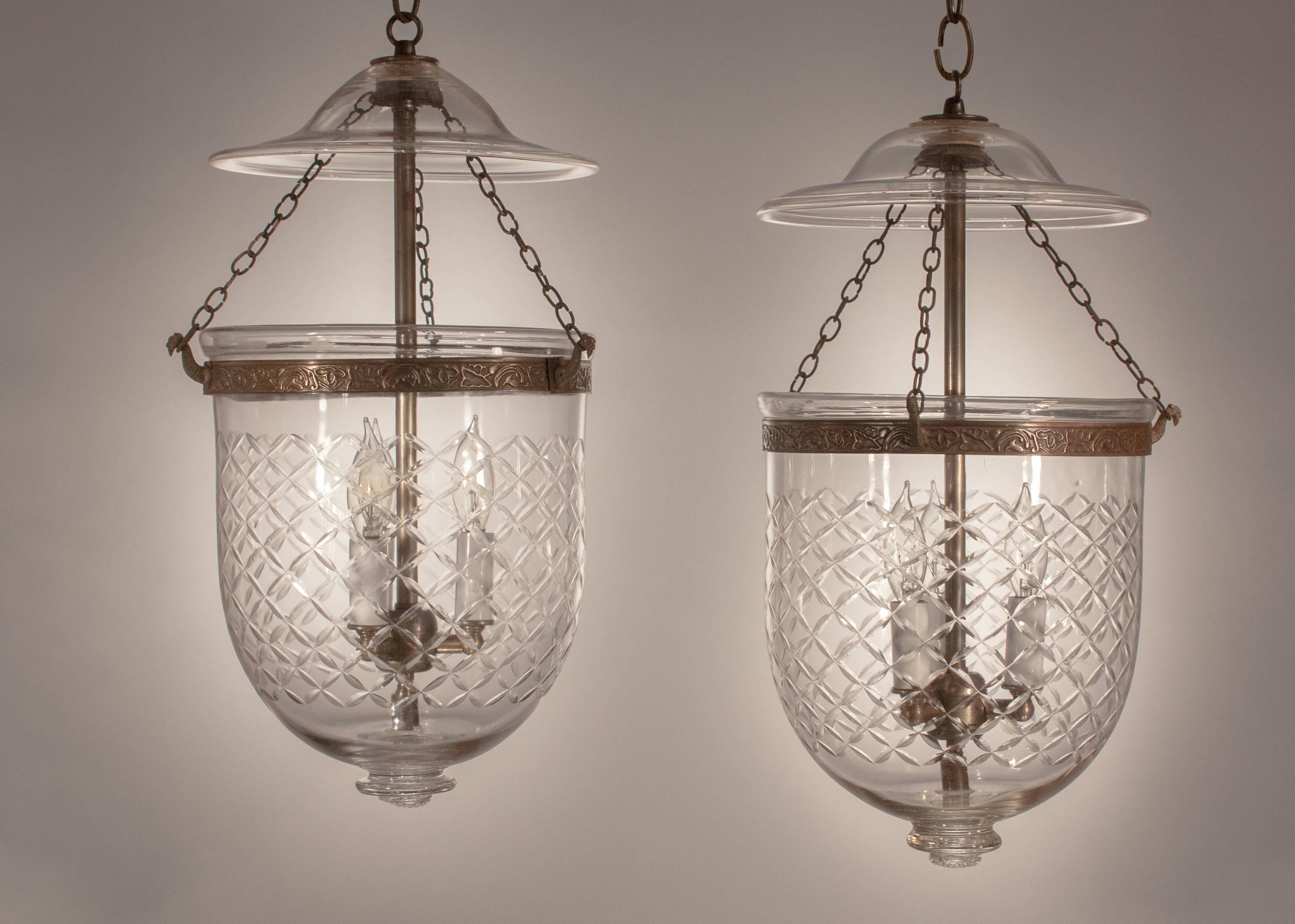 A lovely pair of English handblown glass bell jar lanterns, circa 1870, with a cut-glass diamond etching that complements these medium-sized hall lanterns beautifully. The lanterns have their original smoke bells. The matching brass bands, which