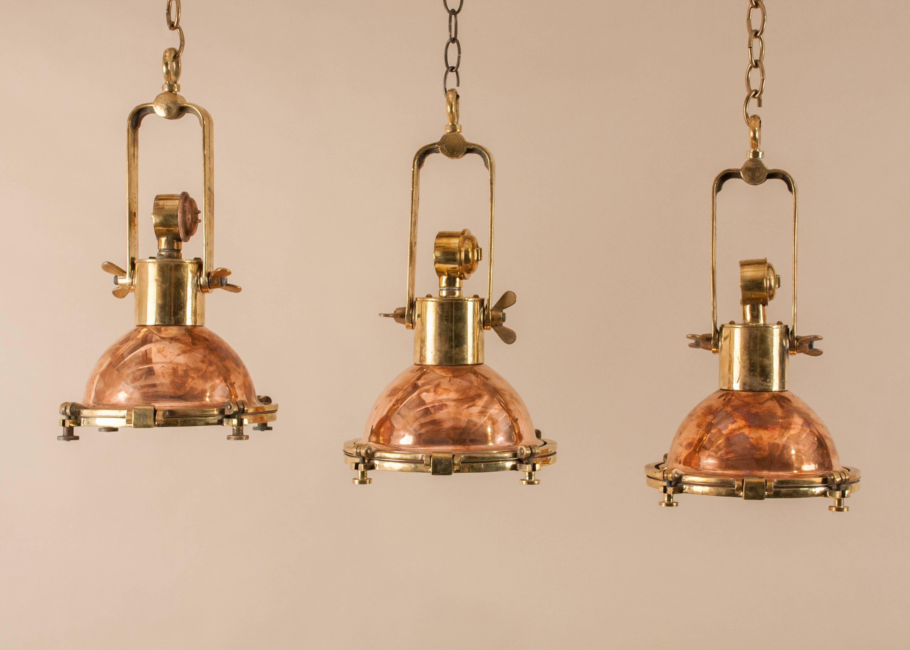 Suite of three petite 1960s copper and brass ship passageway lights with great proportions and patina. Salvaged from a maritime vessel and restored to near-original condition, these authentic nautical pendants have interior steel reflectors and