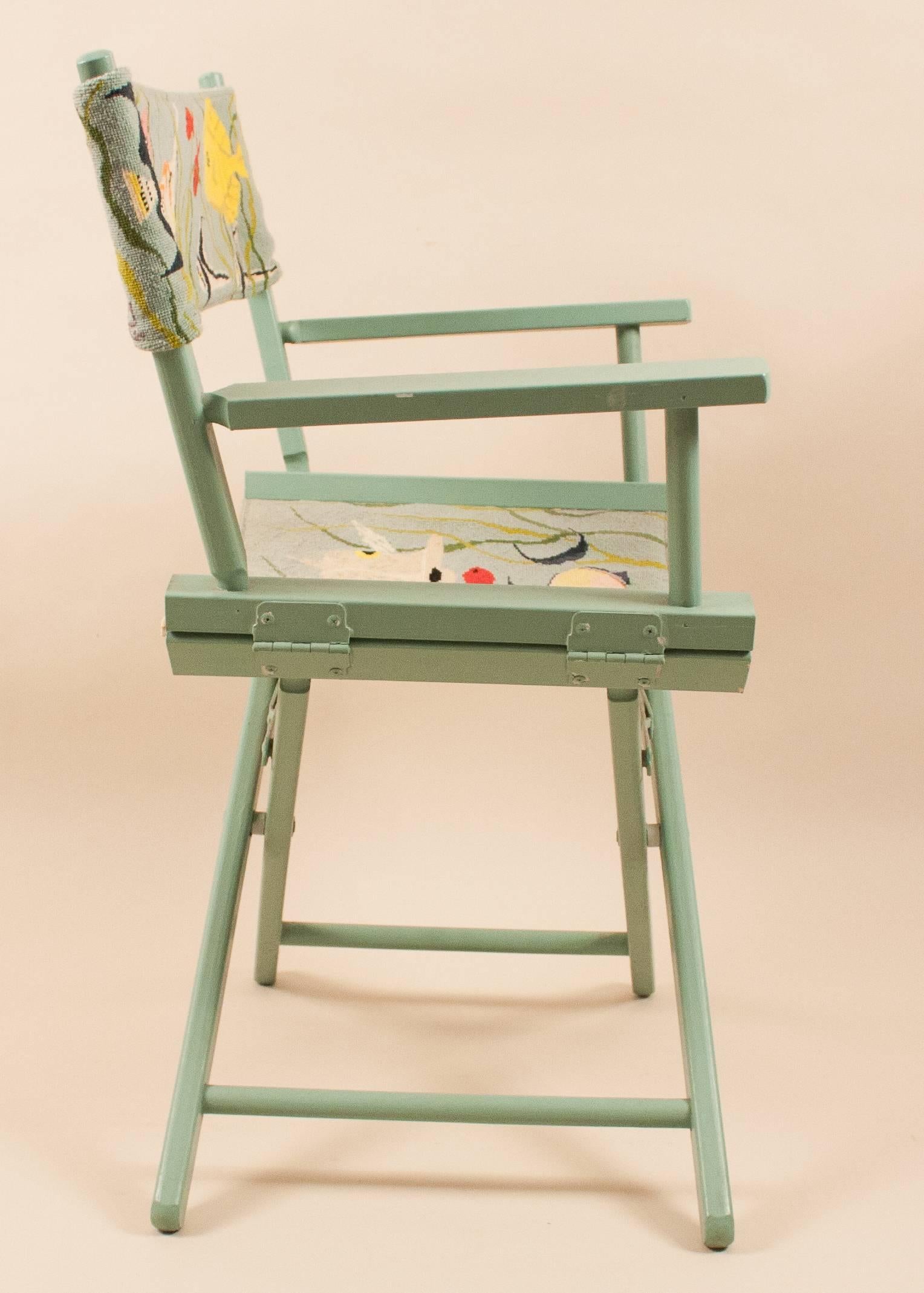 A cheerful mint-colored painted director's chair with hand needlepoint of colorful tropical fish in a reef scene. The handwork is signed with a stitched 