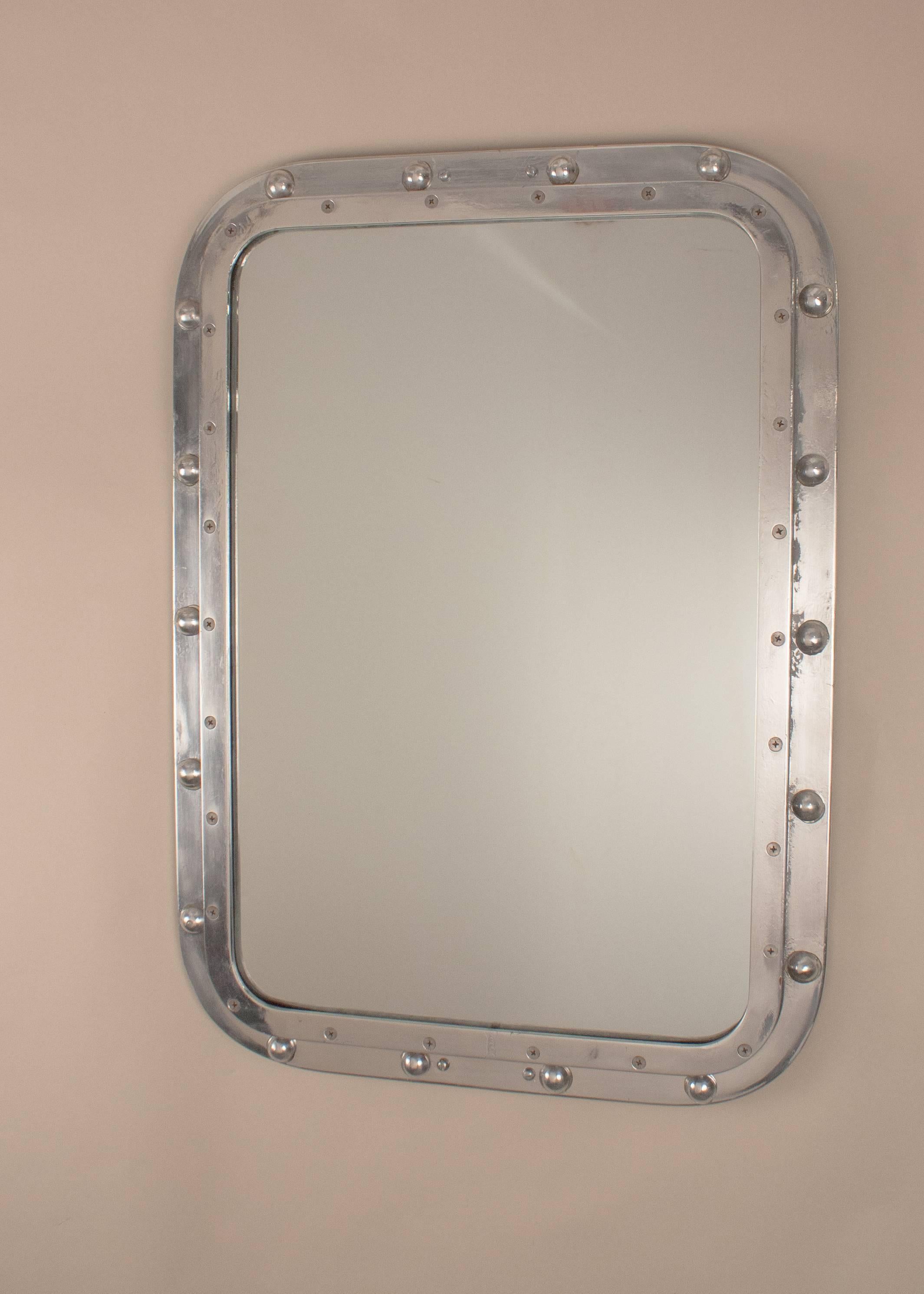 A solid aluminum ship's window wall mirror, circa 1960, that has been salvaged and restored from a mid-century maritime vessel. This rectangular nautical mirror has its original circular rivets and screws. It has a clean, modern, industrial
