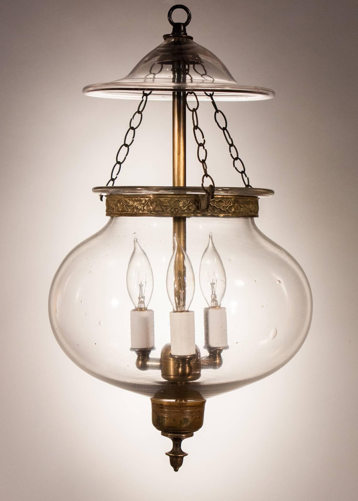 Charming clear glass hall lantern from England, circa 1860, with its original embossed brass band and candleholder finial base. The globe is quite shapely and has desirable swirls and air bubbles in the handblown glass. Several surface scratches are