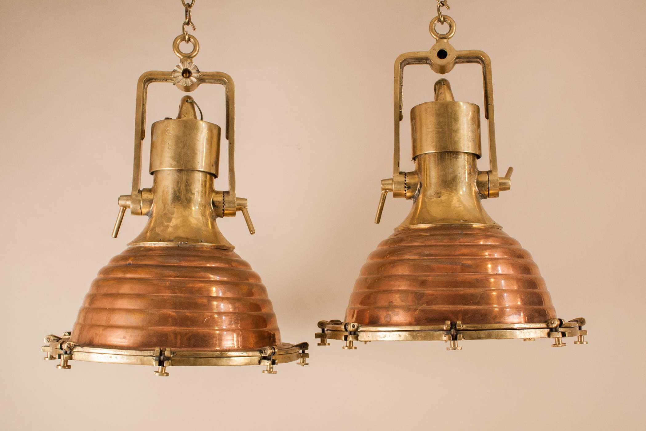 An authentic pair of large copper and brass ship deck lights with great form and patina. These nautical pendants have fluted exteriors, copper reflective interiors and tempered glass lenses. Manufactured in Germany by Wiska, circa 1960, the