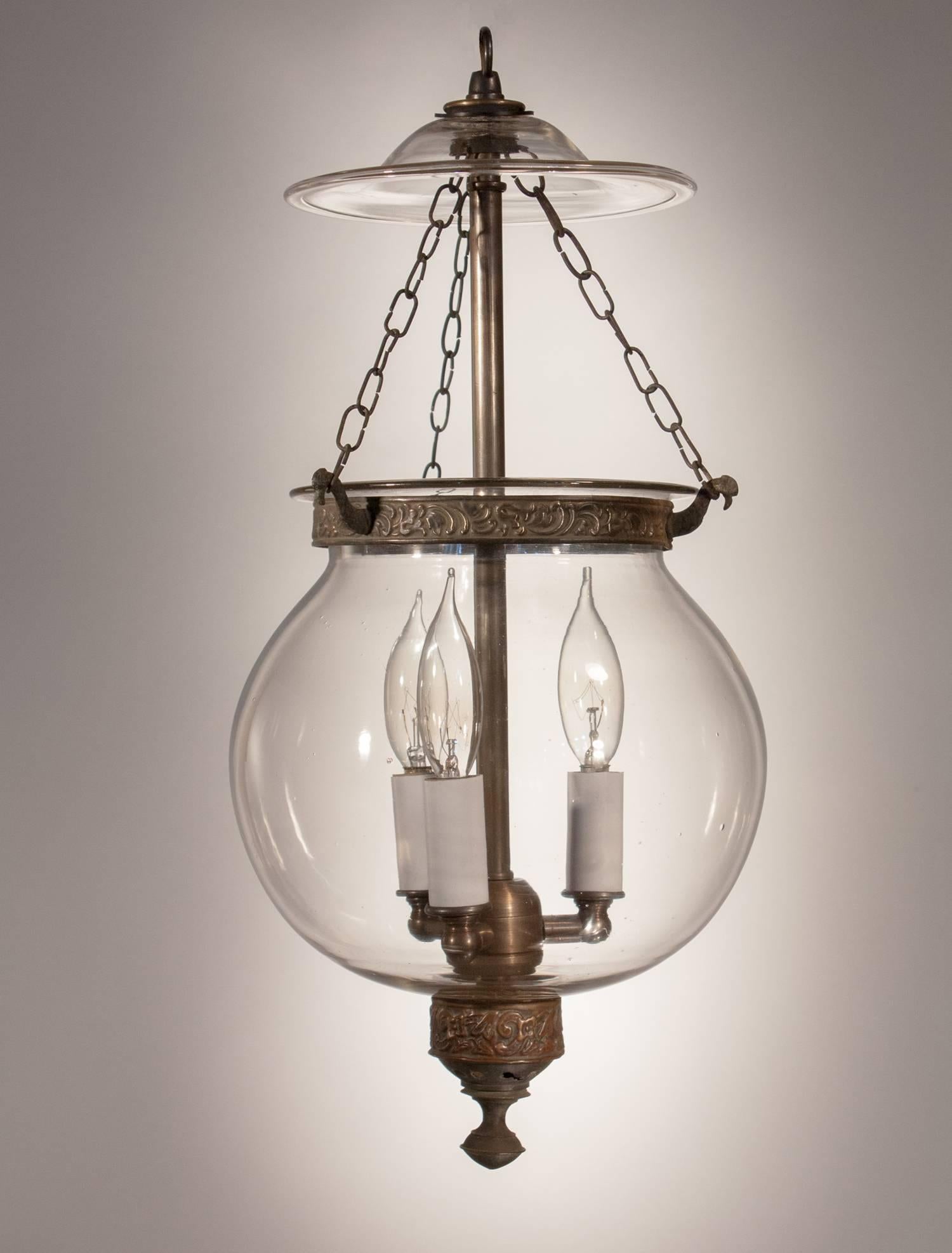 Charming clear glass hall lantern from England, circa 1860, with its original embossed brass band and candle holder finial base. The globe has a lovely shape and several desirable air bubbles in the hand blown glass. It has been newly electrified