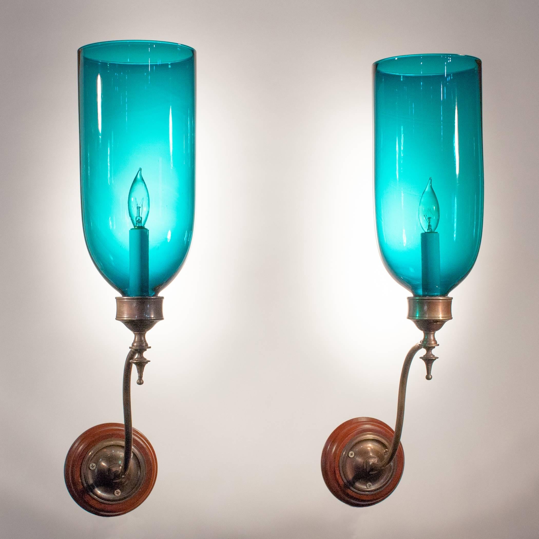 A rare pair of 19th century English hurricane sconces with a beautiful teal blue-green hue. These antique shades have desirable swirls and air bubbles that speak to the quality and age of the hand blown glass. The wall sconces are newly electrified,