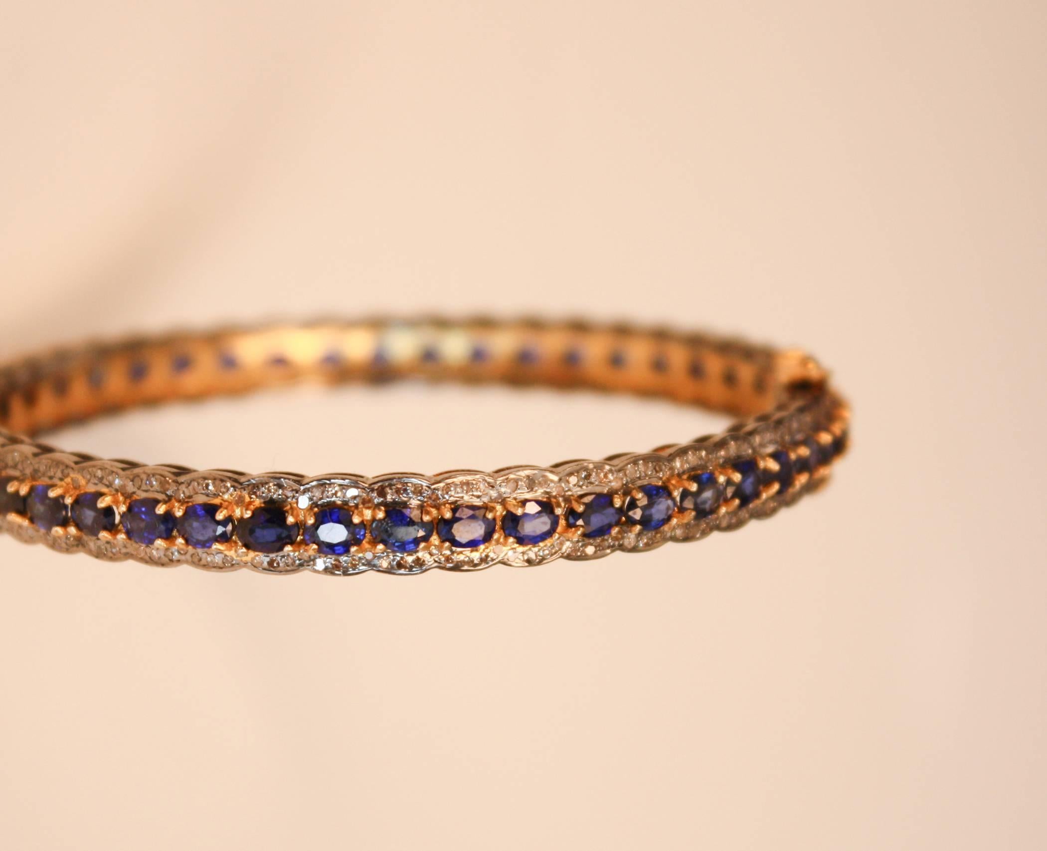Faceted blue sapphires surrounded by single cut, pave set diamonds adorn this wearable bangle. The gems are set in sterling silver and the inside of the bracelet is gold vermeil. The safeties are 14k gold.
Inside diameter: 2.25