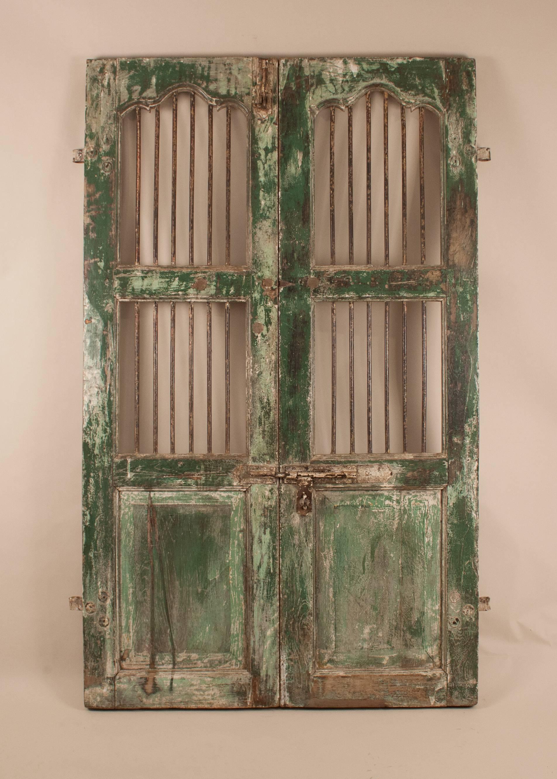 A rustically beautiful green painted courtyard gate from India, circa 1930, carved from teak wood with original, hand wrought iron bars and working double bolts. These colorful door panels have great patina and offer a wealth of interior and