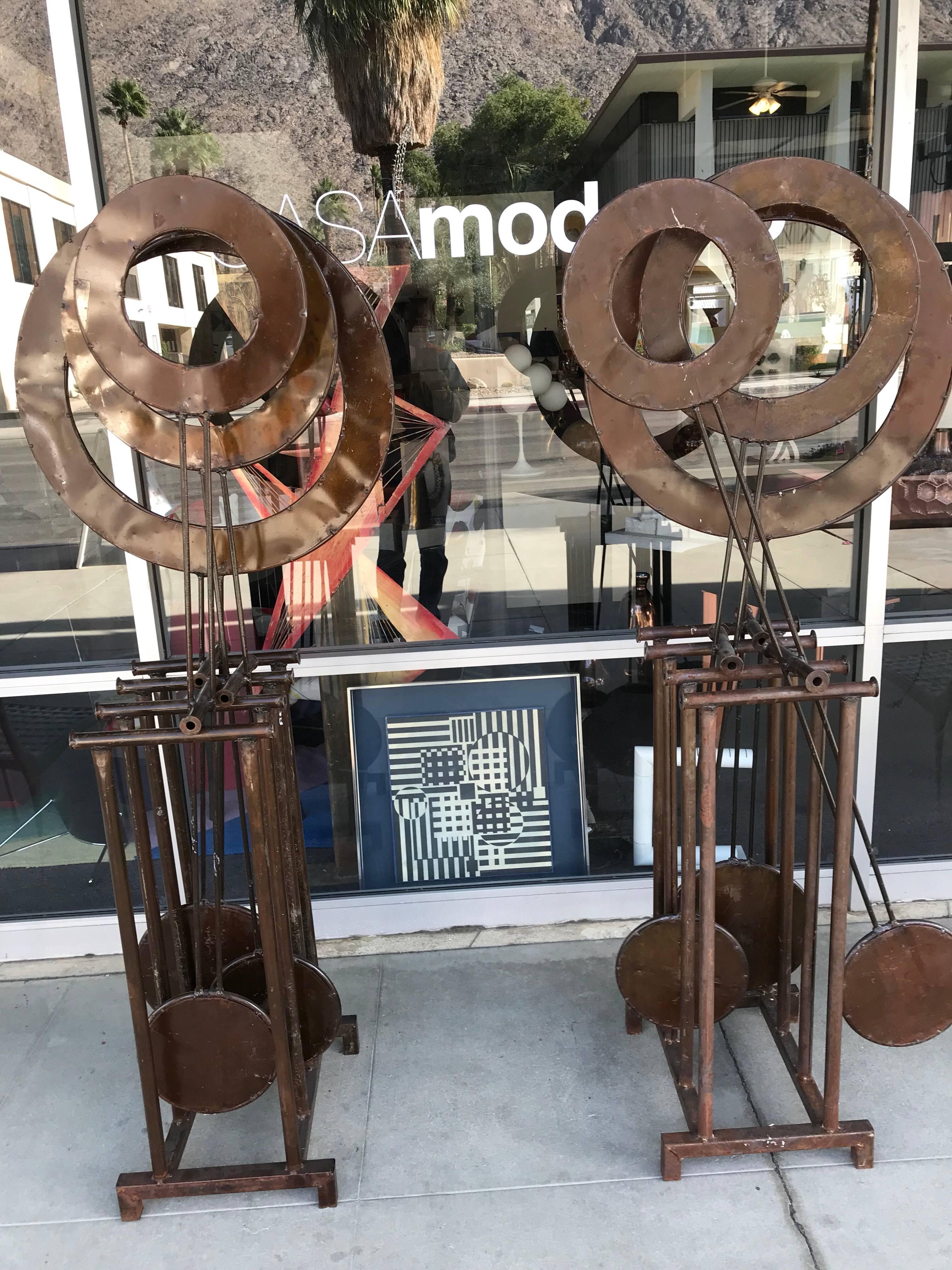 These metal kinetic sculptures made circa 1990, were from a Palm Springs Estate and used outside in a covered entrance (one on each side of their double doors) They have a brown Brutalist colored metal finish. They move with wind or can be started