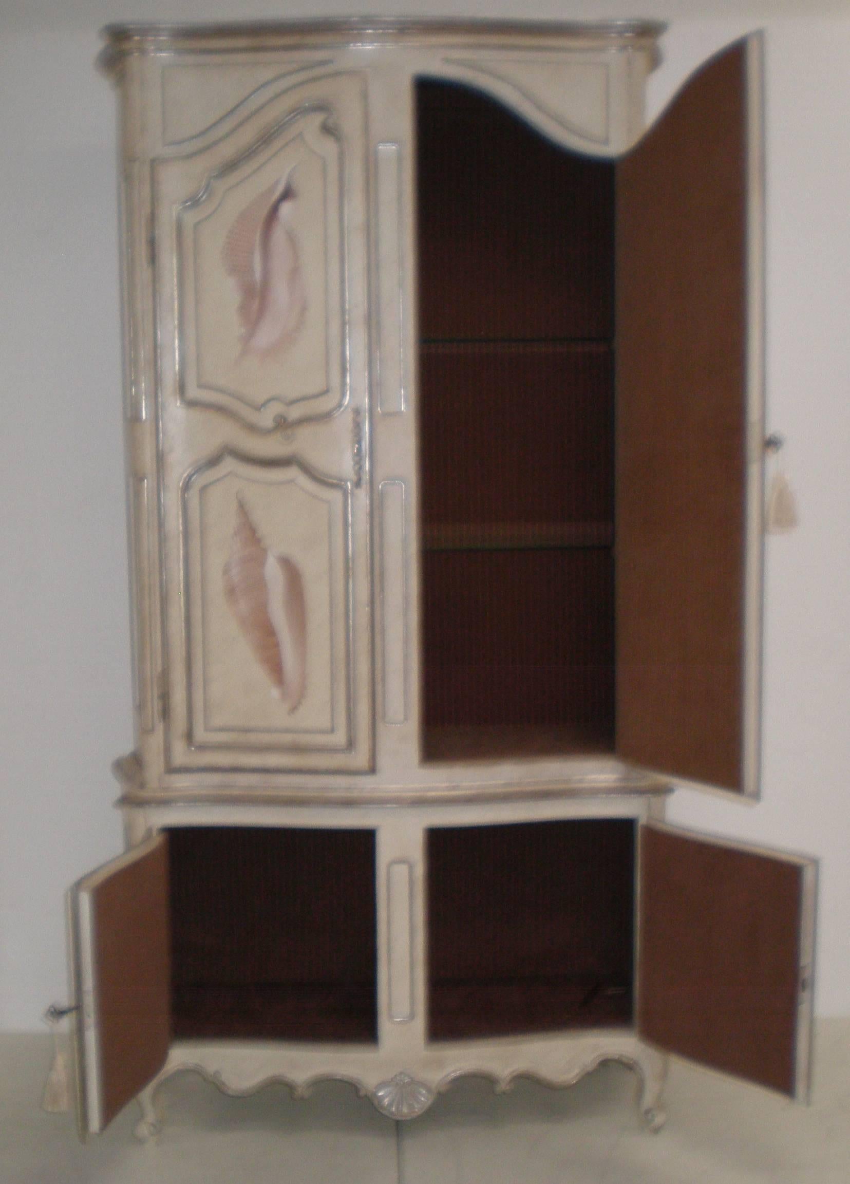 Custom-made, original painting of unique assorted shells by listed artist, Lucien Horton, this tall four-door, two-piece cabinet is lined in brown ribbed fabric and illuminates with hidden light bulbs on the inside. Two glass shelves on top portion