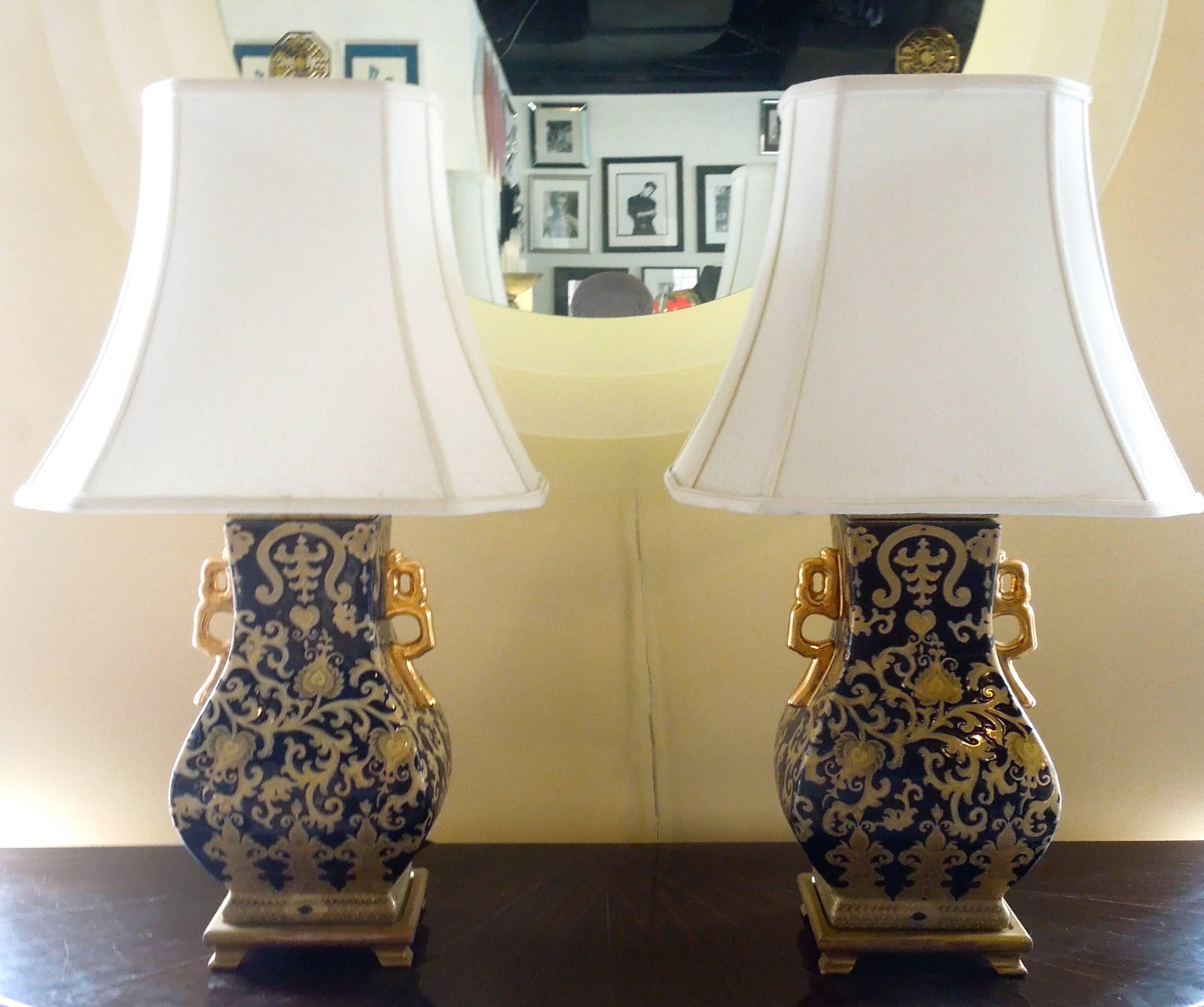 From the master bedroom of a very upscale Palm Springs estate, a chic pair of dark navy and gold ceramic chinioserie lamps. Beautiful gilt handles on each side of the urns. Antique gold wood bases. Obtain original chinioserie shades and Chinese