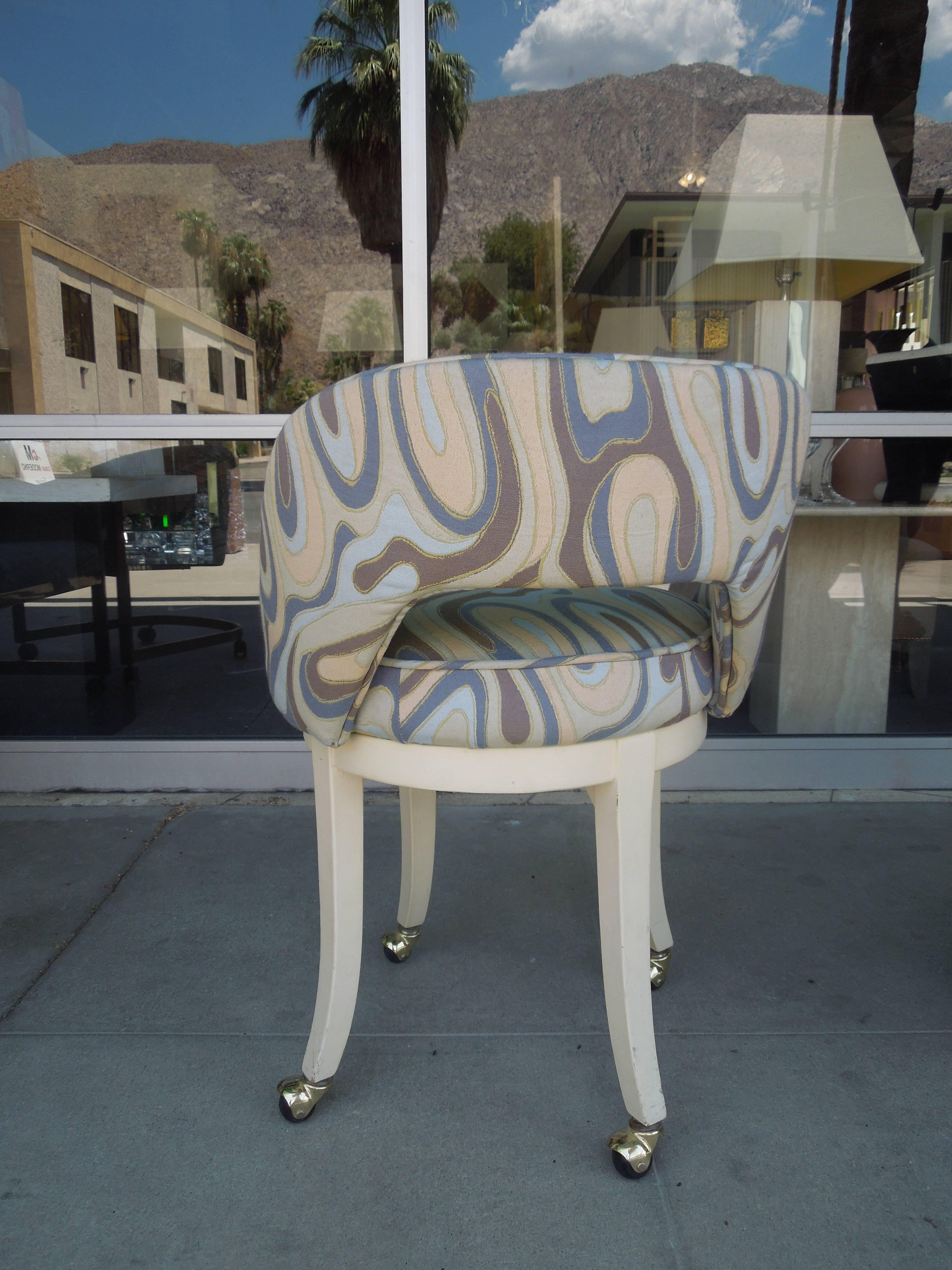 This Palm Springs swivel vanity stool has been reupholstered in a very high end Italian Pucci-esque jacquard fabric with piping just like on the original. Antique white wood base is original on four casters. The seat also swivels. Very chic and