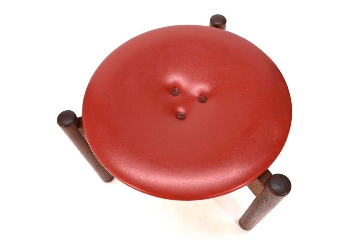 Ottoman or stool in solid teak and red leather designed by Uno and Osten Kristiansson for Luxus of Sweden in the 1960s. This piece has been cleaned and the wood has been oiled, but it is all original and in very nice condition with light wear from