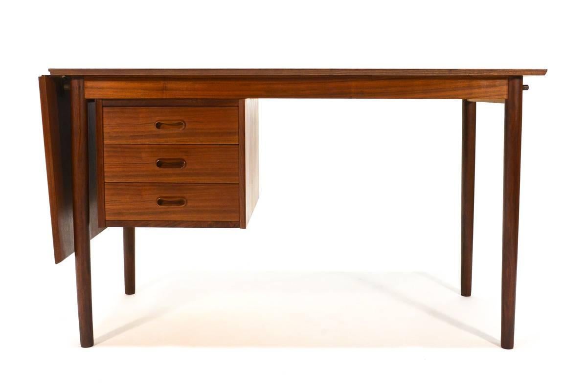 This compact teak desk was designed by Arne Vodder in the 1960s and manufactured by H. Sigh & Sons in Denmark. The desk includes a drop-leaf that allows the top to expand from 47
