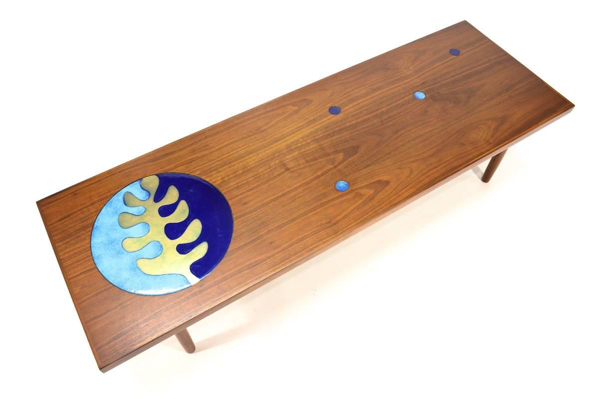 A very unique coffee table. Beautiful walnut top with inset enameled copper discs, sitting on round walnut legs. The large enamel disc is 14