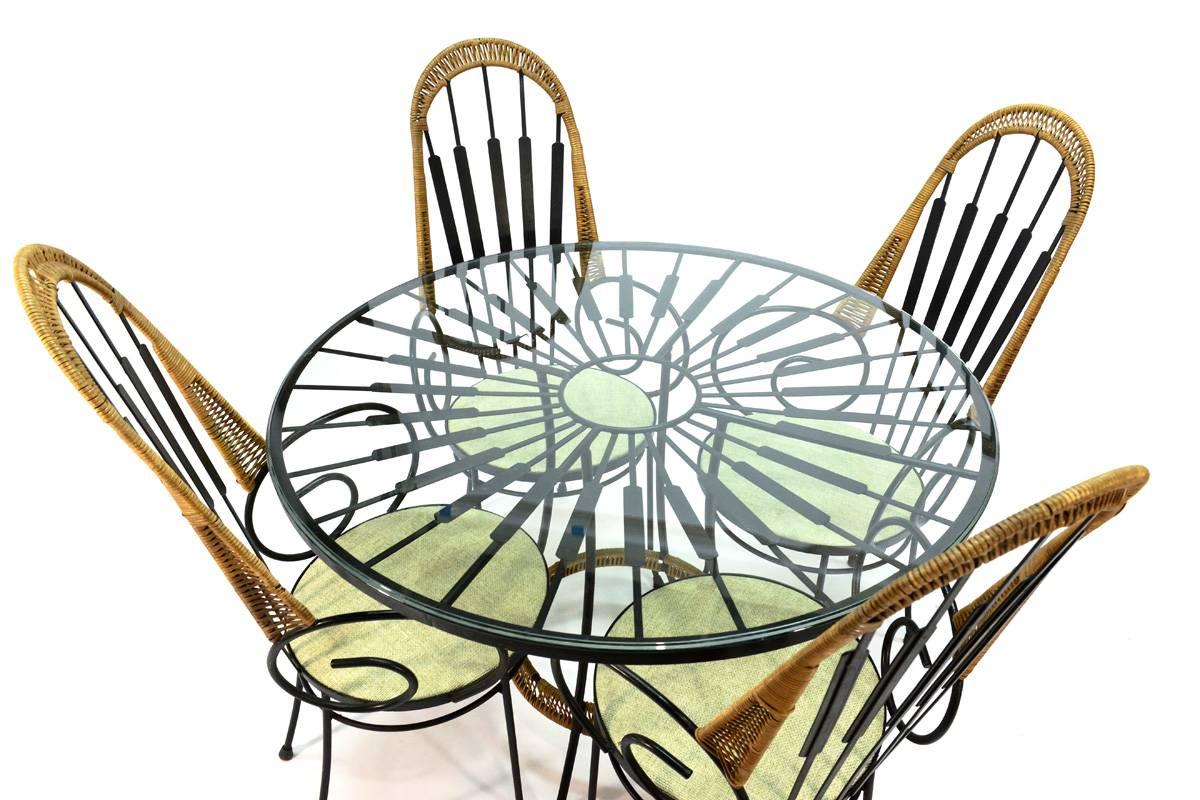 Very fun dining set designed by Arthur Umanoff for Shaver Howard. Iron frames with rattan wrap detailing. In very nice original condition with new upholstery. The cane shows some wear where the chairs contact the table, and there is a small piece