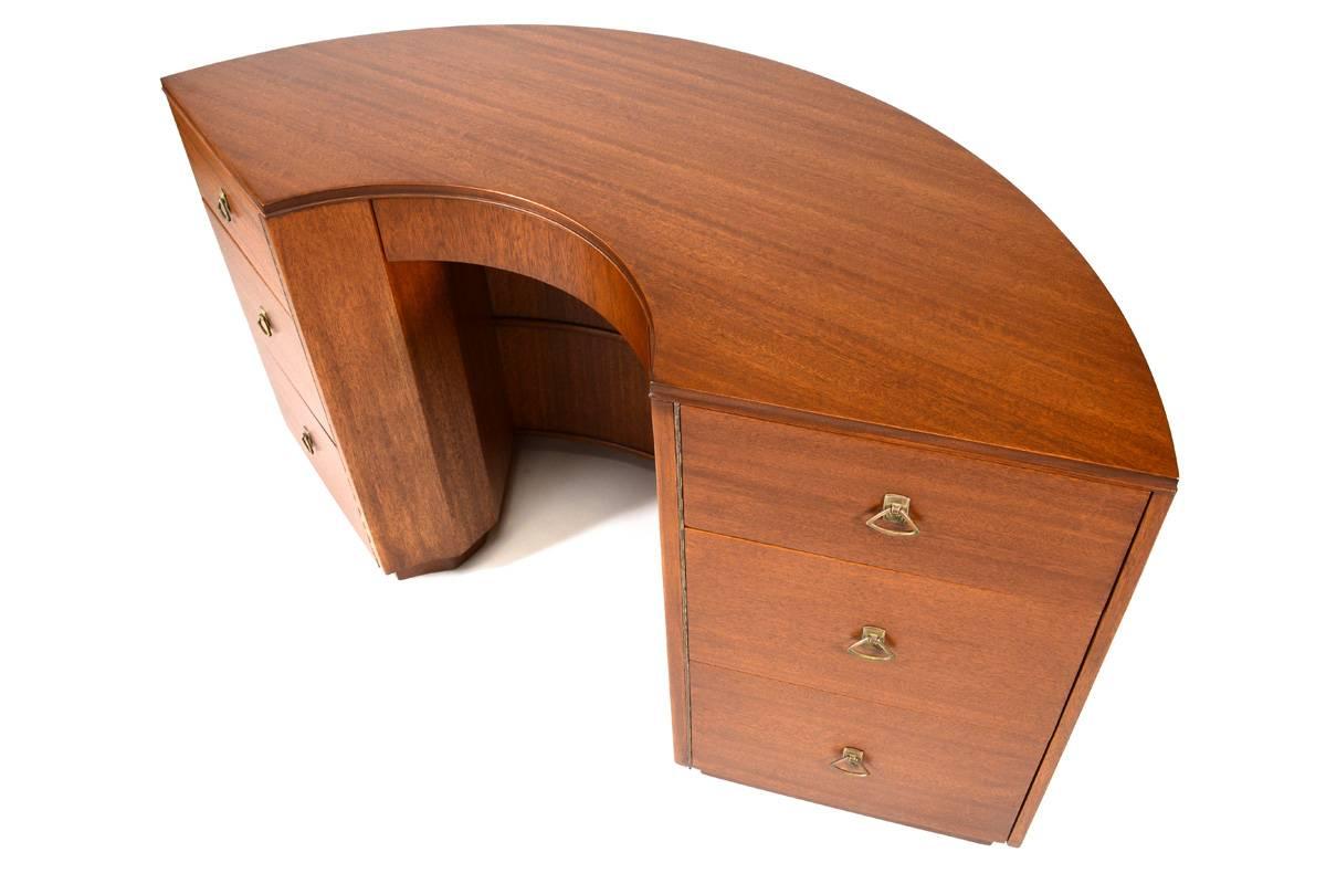 An uncommon and unusual crescent desk designed by Gilbert Rohde for Brown Saltman of California in the 1930's. Beyond its curved shape this piece has some unique features like the pivoting drawers and the inset bookshelf on the backside. The golden