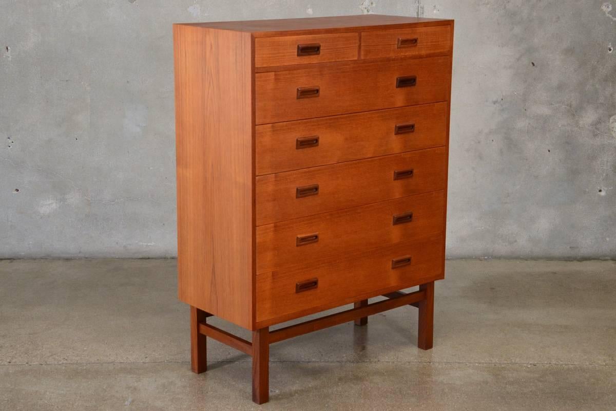 One of a pair we currently have available, this Danish teak high boy dresser offers ample storage with Classic Minimalist styling reminiscent of Borge Mogensen. The five spacious full width drawers and two small top drawers are accent with sculpted