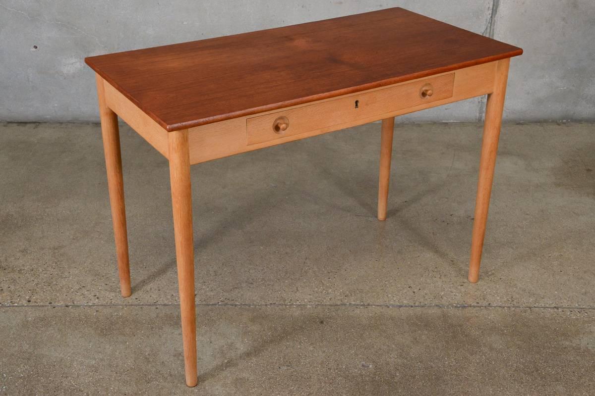 An uncommon smaller scale writing desk designed by Hans Wegner for RY mobler. Model number RY32, it is referred to as the 'Ladies Desk' because of its petite size. This example features a beautiful teak top over a light oak base with highly