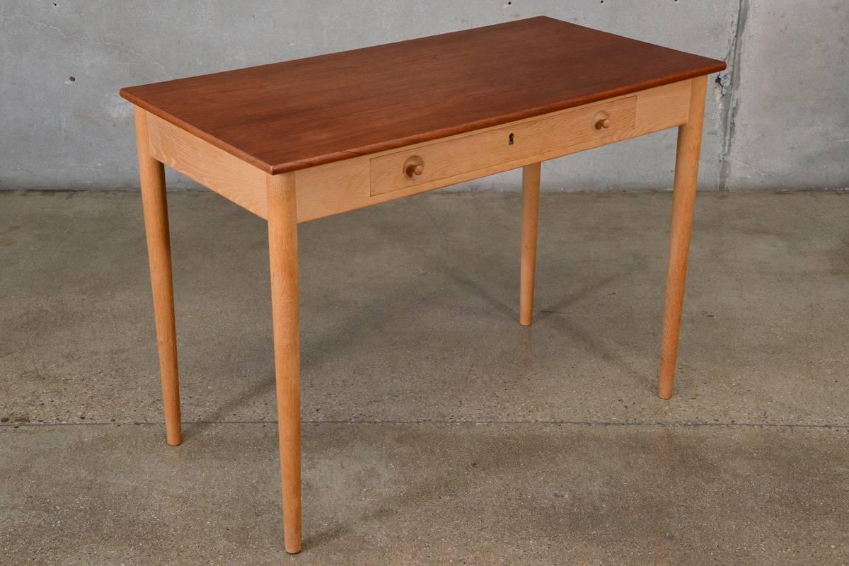 An uncommon smaller scale writing desk designed by Hans Wegner for Ry Mobler. Model number RY32, it is referred to as the 'Ladies Desk' because of its petite size. This example features a beautiful teak top over a light oak base with highly