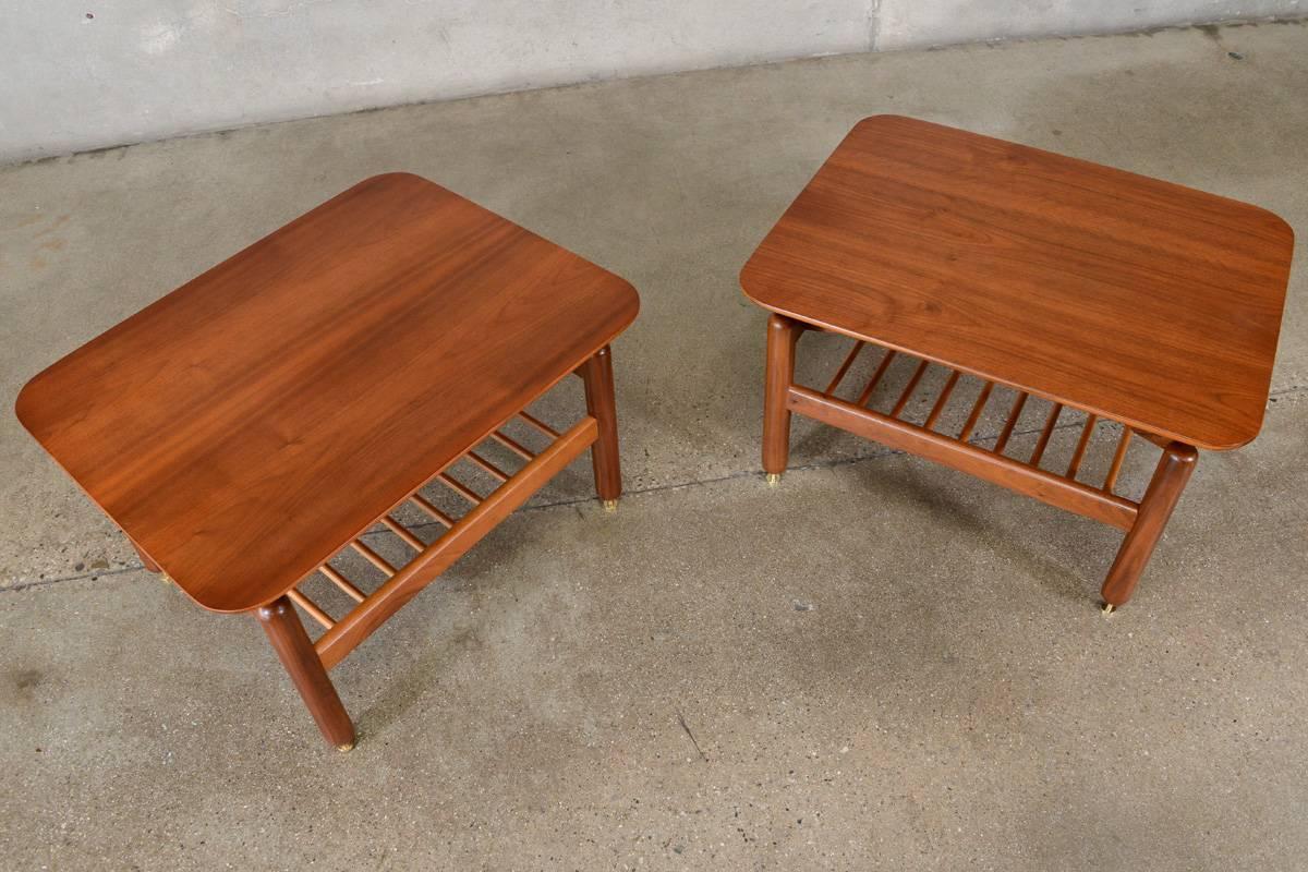 A very nice pair of walnut side tables designed by Greta Grossman for Glenn of California in the 1950s. A simple, not quite square, deign with a dowel lower shelf and unique brass feet. This pair has been completely restored and is in excellent
